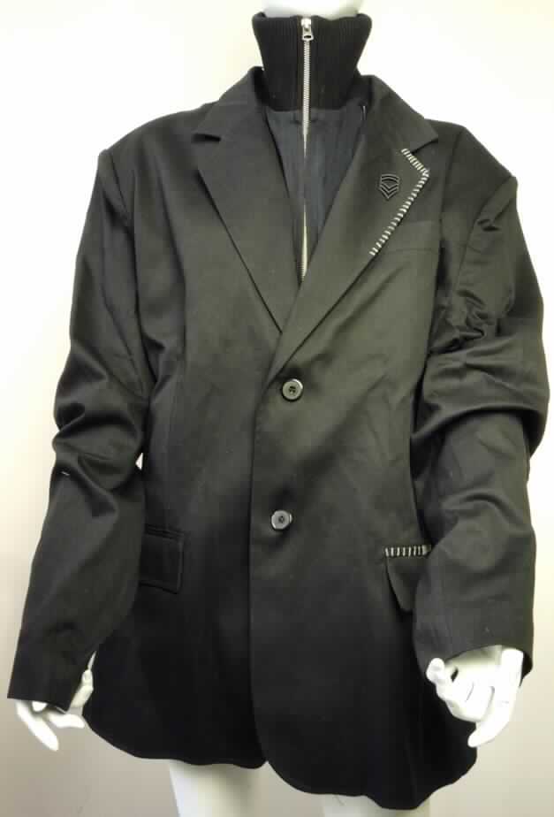 Jacke, sog. Grant Sakko, Größe XL, Foto siehe Anlage,,
- aus 0,6 mm dicken, einfarbigen Geweben aus laut Antrag 98% Baumwolle und 2% Spandex
  (synthetische Chemiefasern),
- vollständig leicht gefüttert, 
- über den Schritt reichend (Rückenlänge: 82 cm), 
- mit einem Reverskragen,
- mit einem durch Reißverschluss an den Vorderteilen und am Kragen befestigten und
  heraustrennbaren Einsatz mit einem gerippt gewirken Stehkragen und einem Reißverschluss,
- vorn mit einer durchgehenden Öffnung, die mit zwei Knöpfen von links über rechts
  geschlossen wird (Männerkleidung), 
- mit langen Ärmeln, 
- mit einer optischen Brusttasche und zwei optischen Taschen mit Patte unterhalb der Taille; 
- in sechs Längsteilen (Bahnen) gearbeitet,
- am unteren Rand gesäumt,
- am Reverskragen mit einem Abzeichen und mit Applikationen, sowie an einer Taschenpatte 
  mit Applikationen verziert,
- wird im Allgemeinen nicht über jeder Kleidung und zum Schutz gegen das Wetter getragen 
  (somit kein den Windjacken ähnliches Kleidungsstück oder Kurzmantel der Position 6201).

"Jacke, aus Geweben, für Männer, aus Baumwolle, keine Arbeits- und Berufskleidung"