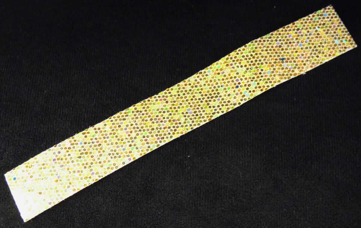 Textillaminat, sog. Dekorationsband zum Aufbügeln mit Glitzer, Foto siehe Anlage,
- als Meterware, mit einer Breite von ca. 2 cm,
- aus drei mit ihrer ganzen Fläche aufeinander liegenden und so miteinander durch Kleben verbundenen Lagen:
-- mit einer Oberlage (Schauseite):
--- aus einem Kettengewirke aus synthetischen Chemiefasern, 
--- ohne Flor- oder Schlingenoberfläche,
--- keine Raschelspitze,
-- mit einer Zwischenlage (Mitte):
--- mittels Kleber auf einem Kunststoff aufgebrachte, metallisierte Kunststoff-Partikel,
-- mit einer Unterlage:
--- aus einem Gewebe aus synthetischen Chemiefasern,
- das die Schauseite bildende Kettengewirke verleiht der Ware insbesondere im Hinblick auf die Verwendung als
  Dekorationsband ihren wesentlichen Charakter.

"Gewirke, mit einer Breite von weniger als 30 cm, anderes als solche der Positionen 6001 und 6002,
 aus synthetischen Chemiefasern, keine Raschelspitze"