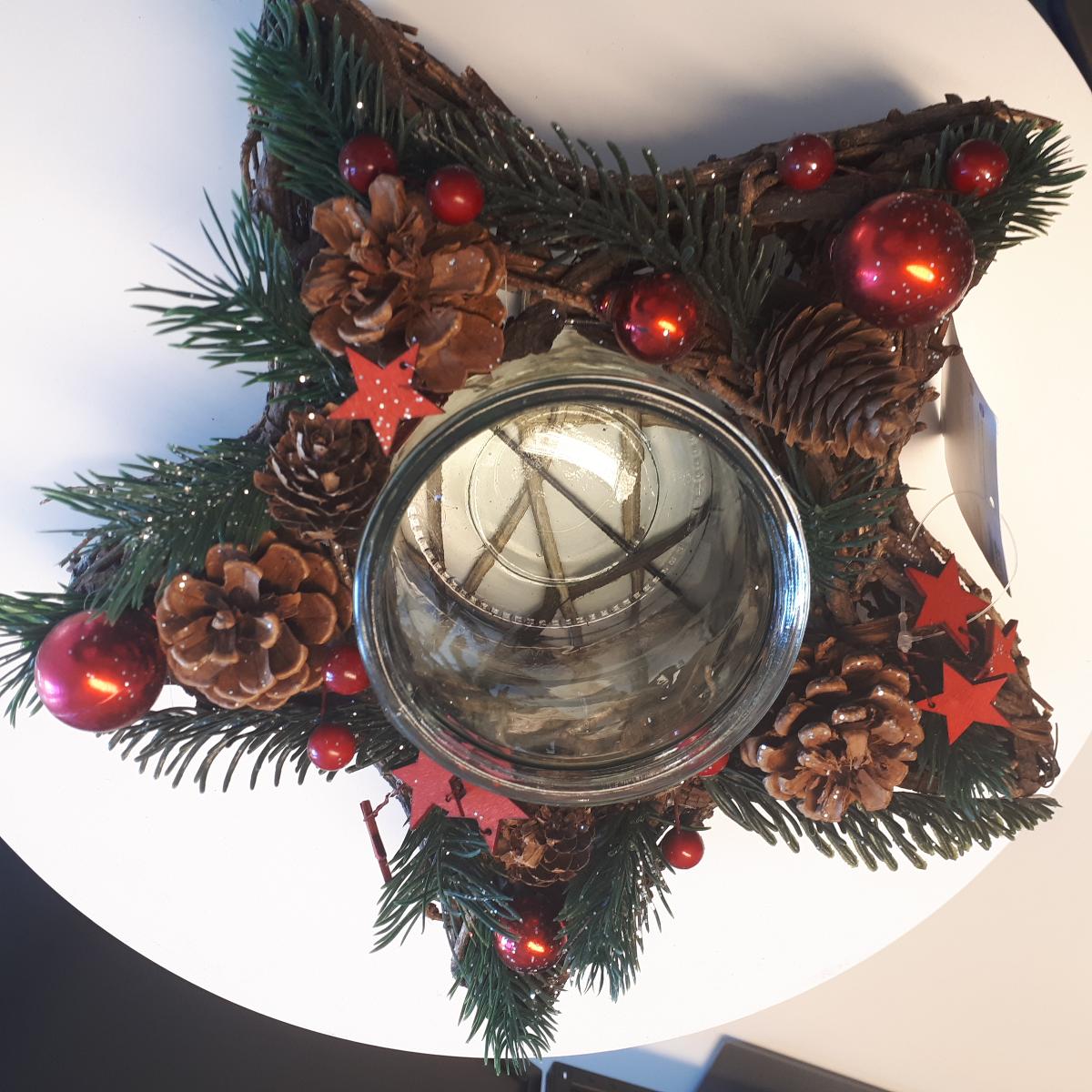 Nach den Angaben der Antragstellerin sowie dem vorliegenden Warenmuster handelt es sich bei dem sog. „Adventsgesteck Stern mit Maxileuchtglas“ um eine zusammengesetzte Ware in Form eines Windlichtes, bestehend aus einem sternförmigen, verzierten Korpus mit einem mittig eingestellten Becherglas.

Der Korpus besteht aus einem formgebenden Gestell aus Metalldraht (H 6 cm x D 28 cm), dass auf der Außenseite nahezu blickdicht mit dünnen, biegsamen Zweigen und Pflanzenstreifen (Flechtstoffe im Sinne der Anmerkung 1 zu Kapitel 46) umflochten und mit dünnen Drähten fixiert ist. Die Oberseite des Sternes ist zur Erhöhung der Zierwirkung mit getrockneten Kiefernzapfen, künstlichen Tannenzweigen, Nachbildungen von roten Beeren, Nachbildungen von roten Christbaumkugeln und sternenförmigen Sperrholzzuschnitten verziert sowie mit Glitzerpartikeln bestäubt.

Das eingestellte, oben offene Behältnis besteht aus augenscheinlich gewöhnlich gefertigtem Glas und weist eine zylindrische Form mit leicht verdicktem Rand auf (H 10 x D 10 cm). Das Glas dient der Aufnahme einer Kerze oder eines Teelichtes (nicht Gegenstand des Gutachtens).

Eine Einreihung des Windlichtes als Beleuchtungskörper in die Position 9405 kommt nicht in Betracht, da das Glasgefäß weder eine passgenaue Aufnahmevorrichtung für ein Teelicht, noch eine spezielle Haltevorrichtung (Dorn, Klammer oder Klemmvorrichtung) für eine Kerze aufweist.

Der Charakter der zusammengesetzten Ware wird im Hinblick auf die Bedeutung für die Verwendung und das äußere Erscheinungsbild durch den maschinell hergestellten Stern bestimmt. Insbesondere im Hinblick auf den Umfang und das äußere Erscheinungsbild sind hier die Flechtstoffe als charakterverleihend anzusehen.

Zolltarifrechtlich handelt es sich um eine "Andere Ware, unmittelbar aus anderen pflanzlichen Flechtstoffen als Bambus oder Rattan hergestellt, keine Flaschenhülsen aus Stroh, nicht handgearbeitet".