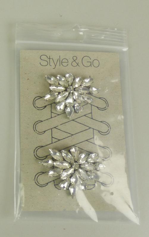 Sogenannter Schmuck für Schuhe (STYLE & GO CLIP 6 'clear flowers):

Es handelt sich um aus unedlem Metall gefertigte Zierelemente für Schuhe in Form einer stilisierten Blume, 2 Stück auf einer Pappkarte. Auf einem runden, flachen Stück aus unedlem Metall sind in unedles Metall eingefasste Kunststoffsteine aufgebracht. An der Unterseite der Waren befindet sich ein Clip, mit dem das Shoe-Accessoire an Schuhbändern, Schnürsenkeln oder auch direkt an der Oberseite von Schuhen befestigt werden kann. 
 - Antragstellerangaben -
Abbildung siehe Anlage.

Nach Umfang und Bedeutung für die Verwendung sind die unedlen Metalle charakterbestimmend (sie bestimmen die Formbgebung und dienen der Befestigung).

Eine Einreihung als Schuhteile in die Position 6406 kommt nicht in Betracht, da die Waren sich als Zier-/Schmuckwaren darstellen.

Derartige Erzeugnisse gehören als "anderer (als in den TARIC-Codes 7117 1100 00 und 7117 1900 10 genannter) Fantasieschmuck, aus unedlen Metallen" zum TARIC-Code 7117 1900 90.