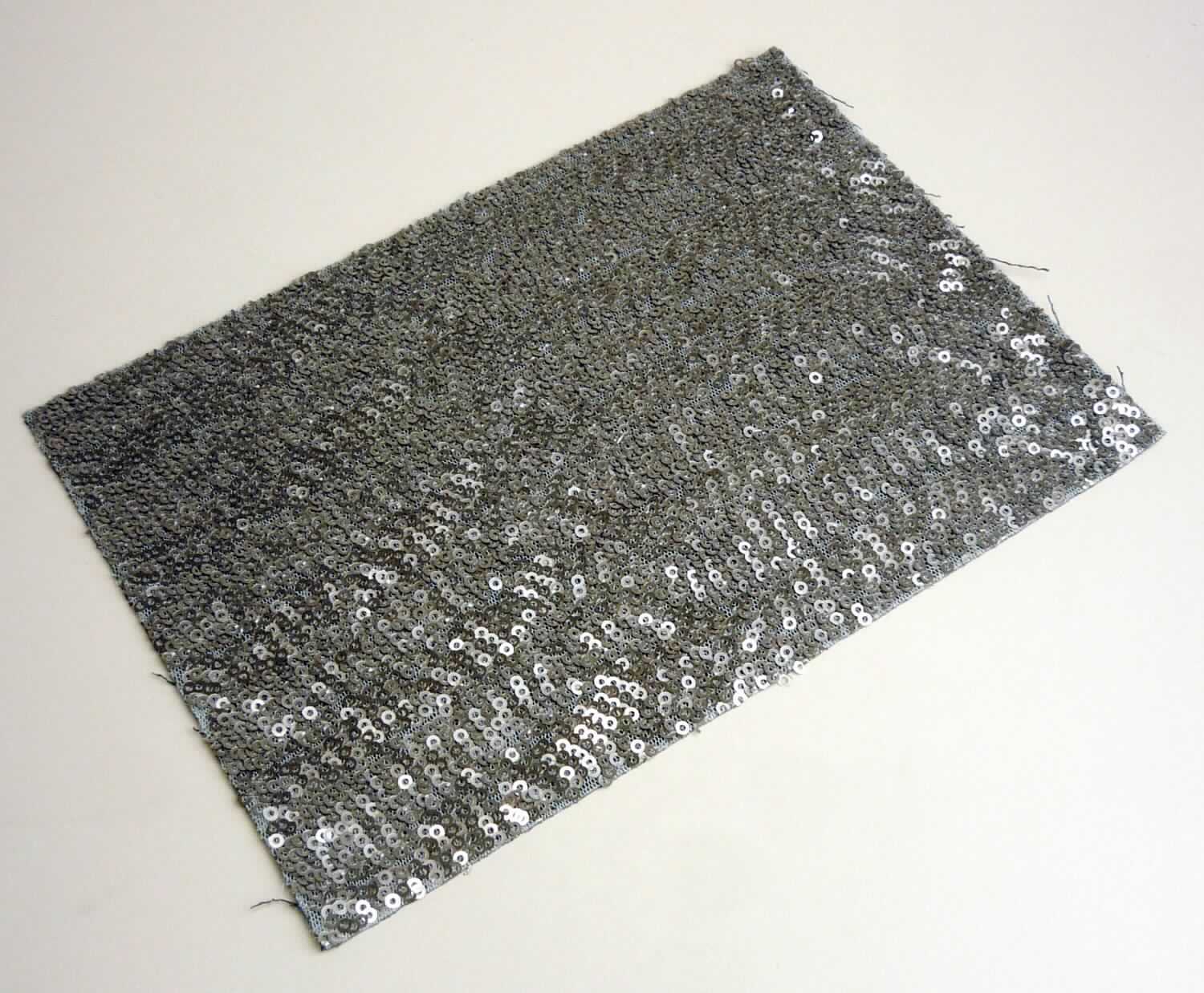 Textillaminat, sog. Stoff, Foto siehe Anlage,
- als Meterware, mit einer Breite von laut Antrag 125 cm,
- laut Untersuchungsergebnis:
-- aus zwei mit ihrer ganzen Fläche aufeinander liegenden und so miteinander durch Kleben verbundenen Lagen:
-- mit einer Oberlage (Schauseite):
--- aus einer Applikationsstickerei mit einem Stickgrund aus Kettengewirken aus synthetischen Chemiefasern
    (laut Antrag: Polyester),
--- mit aufgestickten Kunststoff-Pailletten (Applikationen),
--- maschinell hergestellt,
--- keine Ätzstickerei,
--- mit einem Wert von laut Antrag mehr als 17,50 Euro je kg Eigengewicht,
-- mit einer Unterlage:
--- aus einem gefärbten Gewebe aus laut Antrag Baumwolle,
--- in Köperbindung,
- die die Schauseite bildende Stickerei verleiht der Ware insbesondere im Hinblick auf das äußere 
  Erscheinungsbild ihren wesentlichen Charakter.

"Stickerei als Meterware, keine Ätzstickereien und Stickereien mit herausgeschnittenem Grund, aus Chemiefasern,
 mit einem Wert von mehr als 17,50 Euro je kg Eigengewicht, nicht handgearbeitet"