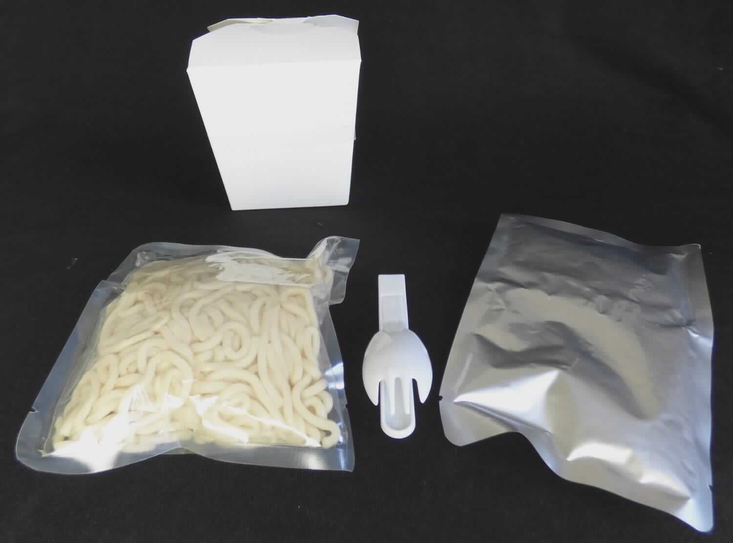 Instant Nudelgericht Bami Goreng

Ein Warenmuster (nicht in Originalumschließung) sowie eine Produktspezifikation lagen vor.
Nach den Antragsangaben wird das Erzeugnis fertig konfektioniert zur Abgabe an den Endverbraucher in die Gemeinschaft eingeführt.
Demzufolge handelt es sich um eine Warenzusammenstellung in Aufmachung für den Einzelverkauf (insgesamt 280 g), bestehend aus einem Beutel mit vorgekochten, beigefarbenen, feuchten, leicht fettigen Teigwaren und einem Beutel mit einer rotbraunen, rote Chili- und Hühnchenfleischstücke enthaltenden Würzsauce. Beides ist verpackt in einer sogenannten Heat & Eat Box, in der die beiden Bestandteile in einer Mikrowelle 1 - 2 Minuten erhitzt werden sollen. 
Beigelegt ist eine zusammensteckbare Einweg-Kunststoffgabel.

Es liegt eine Warenzusammenstellung in Aufmachung für den Einzelverkauf gemäß AV 3b) vor, die zur Herstellung eines Nudelgerichts vorgesehen ist. Der Charakter wird durch die Nudeln bestimmt, da diese den größten Teil der Ware ausmachen.

Teigwaren, gekocht, nicht gefüllt und nicht getrocknet, keinen Reis enthaltend.