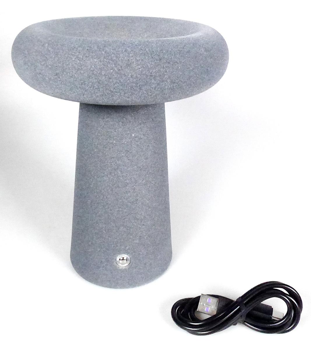 Bei der sog. LED-Donutlampe handelt es sich um eine ca. 185 mm hohe elektrische Tisch-/Nachttischleuchte in drei Designs (Art. 9075956 gelb, Art. 9070557 sandgrau und Art. 9076555 dunkelgrau) zur Verwendung in Innenräumen, im Wesentlichen bestehend aus einem runden konischen Lampenfuß aus Metall mit einer Filzbeschichtung an der Außenseite, einem kreisrunden (d: ca. 140 mm; H: ca. 35 mm), an der Oberseite mit einer Delle versehenen Lampenschirm aus gleichem Material mit integrierter im Dauerlicht weiß leuchtender, in drei Stufen dimmbarer LED-Lichtquelle und einer weißen transparenten, an der Unterseite des Lampenschirms angebrachten Leuchtmittelabdeckung aus Kunststoff.
Die Leuchte ist mit Batteriebetrieb, einem USB-Anschluss und einem Berührungssensor (Ein-/Ausschalter und zur Einstellung der Helligkeitsstufen) ausgestattet.
Sie wird mittels beigefügtem USB-Ladekabel aufgeladen.

Die Bestandteile aus Metall (Umfang und Bedeutung für die Verwendung als stabilitätsverleihendes Element) und Spinnstoff (äußeres Erscheinungsbild) bestimmen gegenüber dem Kunststoff den stofflichen Charakter der Leuchte. 

Hinweise auf Handarbeit liegen nicht vor.

Das Erzeugnis ist als "Leuchte, anderweit weder genannt noch inbegriffen, elektrische Tisch- bzw. Nachttischleuchte, ausschließlich zur Verwendung mit LED-Lichtquellen bestimmt, aus Metall und Spinnstoff, nicht handgearbeitet" einzureihen.