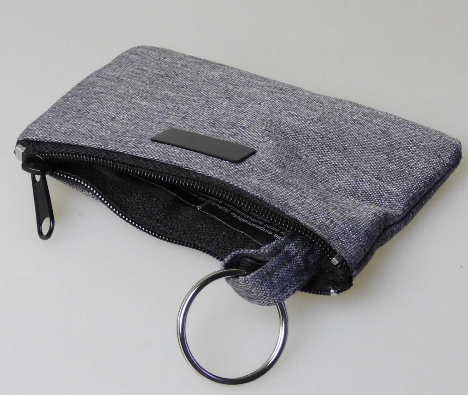 Ähnliches Behältnis (Schlüsseltasche), Taschen- oder Handtaschenartikel, sog. Schlüsseltasche, 
Art.-Nr. 244-58.014, Abbildung siehe Anlage, 
- mit einer Außenseite aus Spinnstoffen, 
- mit einem Reißverschluss entlang des oberen Randes zu öffnen, 
- innen mit einem Schlüsselring (Durchmesser ca. 3 cm) aus unedlem Metall, befestigt an einer Spinnstofflasche, 
  zur Aufnahme der Schlüssel; gefüttert, 
- mit einer sog. RFID-Abschirmung, 
- mit den Abmessungen von ca. 11 cm (Breite) x 7,5 cm (Höhe) x 1 cm (Tiefe), 
- keine Hinweise auf Handarbeit.

"Ähnliches Behältnis (Schlüsseltasche), Taschen- oder Handtaschenartikel, mit Außenseite aus Spinnstoffen, nicht 
 handgearbeitet"