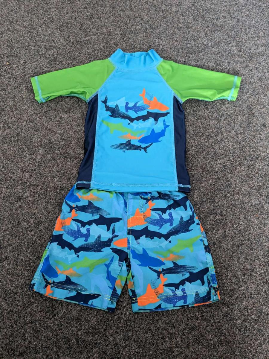 Unterziehpulli und Badehose, sog. Bade-Set, Größe 98/104, Foto siehe Anlage,
- laut Antrag jeweils auf einem Kleiderbügel aufgehängt und gemeinsam in einem Polybeutel verpackt,
- als zweiteilige Zusammenstellung,
- kein zweiteiliger Badeanzug, u. a. da das Oberteil aufgrund seines Schnitts nicht erkennen lässt, dass
  es ausschließlich oder hauptsächlich dazu bestimmt ist, als Badekleidung getragen zu werden,
- keine Kombination, u. a. weil die Kleidungsstücke nicht aus ein und demselben Flächenerzeugnis
  hergestellt sind,
- getrennte Einreihung aller Bestandteile, weil die Kleidungsstücke nicht zusammen in eine Position
  eingereiht werden können,
- Unterziehpulli:
- aus ca. 0,5 mm dicken (leichten), einfarbigen bzw. bedruckten Gewirken aus laut Antrag 85 % Polyester
  und 15 % Elasthan (beides synthetische Chemiefasern), mit mehr als 12 Maschen je linearen Zenti-
  meter in jeder Richtung (feinmaschig),
- über die Taille reichend (Rückenlänge: ca. 39,5 cm), 
- mit einem enganliegenden, hohen Kragen (u. a. deshalb kein Kleidungsstück der Position 6109),
- ohne Öffnung und ohne Verschluss,
- mit kurzen, enganliegenden Ärmeln,
- enganliegend gearbeitet (Brustumfang: ca. 53 cm),
- am unteren Rand und an den Ärmelenden durch Umschlagen und Festnähen gesäumt.

"Unterziehpulli, aus Gewirken, aus Chemiefasern"