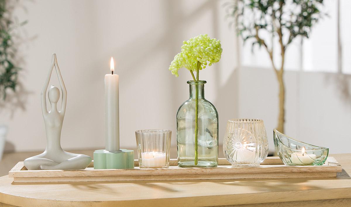 Warenzusammenstellung, bestehend aus drei Windlichtern, einer Vase, einem stilisierten Holunderzweig,
einem Kerzenhalter, einer Zierfigur und einem Tablett, Foto siehe Anlage,
- in Aufmachung für den Einzelverkauf; zur Befriedigung eines speziellen Bedarfs zusammengestellt,
- Windlichter (Glaswaren zur Innenausstattung):
- - oben offene Gefäße aus gewöhnlichem, mechanisch gefertigtem Glas (laut Antrag),
- - unterschiedlich geformt (becherförmig; bauchig; in Schiffchenform)
- - keine nicht elektrischen Beleuchtungskörper der Position 9405, da die Gefäße keine Haltevorrichtung
    oder spezifische Vorrichtung zum Befestigen eines Teelichtes aufweisen,
- Vase (Glasware zur Innenausstattung):
- - aus gewöhnlichem, mechanisch gefertigtem Glas (laut Antrag),
- - in Form einer Flasche mit einem kurzen Hals und einem nach außen gewölbten Rand,
- - mit den Abmessungen: ca. 6 cm (Durchmesser) x 14 cm (Höhe),
- stilisierter Holunderzweig (künstliche Frucht):
- - mit einem verzweigten Stängel aus drei mit Kunststoff ummantelten Drähten aus unedlem Metall,
- - mit beerenartigen Früchten aus Kunststoff; aufgesteckt auf den verzweigten Stängel,
- - durch Stecken in Blumenbindetechnik hergestellt,
- Kerzenhalter:
- - blütenförmige Scheibe aus Holz mit einer Höhe von ca. 3 cm,
- - an der Oberseite mit einer eingesetzten Hülse aus Metall; passgenau zur Aufnahme einer Stabkerze,
- Zierfigur:
- - aus Keramik (laut Antrag),
- - in einer sitzenden Yogapose,
- Tablett:
- - aus Holz (laut Antrag MDF),
- - mit leicht erhöhtem Rand,
- - mit den Abmessungen: ca. 50 cm (Breite) x 12 cm (Tiefe) x 2 cm (Höhe),
- alle Waren sind im Hinblick auf die Zierwirkung gleichbedeutend; die Glaswaren zur Innenausstattung
  bestimmen im Hinblick auf die Menge den wesentlichen Charakter der Warenzusammenstellung.

"Glaswaren zur Innenausstattung, aus gewöhnlichem Glas, nicht handgefertigt"