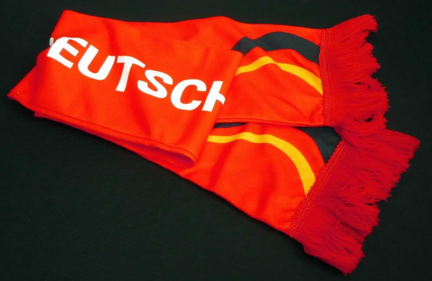 Schal, sog. Fanschal "Fringes" Deutschland, Art. 08648022-00000, in Erwachsenengröße, Foto siehe Anlage,
- rechteckig, in den Abmessungen von ca. 125 cm x 15 cm,
- aus ca. 0,8 mm, bedruckten, einseitig (Außenseite) gerauten Gewirken aus Spinnstoffen,
- schlauchförmig; durch Zusammennähen konfektioniert,
- an den Schmalseiten mit angesetzten Fransen.

"Anderes konfektioniertes Bekleidungszubehör (Schal), aus Gewirken"