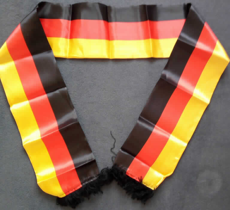 Schal, Art. Nr. 44013, Foto siehe Anlage,
- in einem Polybeutel mit bedrucktem Pappeinleger verpackt,
- aus einem ca. 0,1 mm dicken, bedruckten (schwarz-rot-gold) Gewebe aus laut Antrag Polyester (synthetische
  Chemiefasern),
- doppelt gearbeitet, an den Schmalseiten mit zusätzlich aufgenähten Fransen verziert (u. a. damit konfektioniert);
  in den Abmessungen von: ca. 150 cm x 14,5 cm,
- ohne Hinweise auf Handarbeit,
- auf Grund des verwendeten Flächenerzeugnisses keine Ware aus Kunststoff des Kapitels 39.

"Schal, aus Geweben, aus synthetischen Chemiefasern, nicht handgearbeitet"