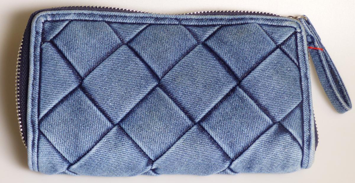 Geldbörse, sog. Graceland Geldbörse 26511/92, Foto siehe Anlage,
- mit einer Außenseite aus Spinnstoffen,
- - Geflecht aus ca. 3,5 cm breiten, geflochtenen Streifen aus Gewebe (kein Flechtstoff im Sinne
    des Kapitels 46),
- mit einem entlang des Rands an drei Seiten umlaufenden Reißverschluss,
- - an beiden Innenseiten mit einem über die gesamte Breite reichenden, offenen Einsteckfach sowie
    mit sechs darauf aufgesetzten Einsteckfächern im Bankkartenformat; mittig mit einem Trennsteg
    in Form eines Reißverschlussfachs (Münzfach) und einem darauf aufgesetzten Einsteckfach
    ausgestattet,
- mit den Abmessungen: ca. 19 cm (Breite) x 11 cm (Höhe) x 3 cm (Tiefe),
- laut Antrag nicht handgearbeitet.

"Geldbörse, Taschen- oder Handtaschenartikel, mit Außenseite aus Spinnstoffen, nicht handgearbeitet"