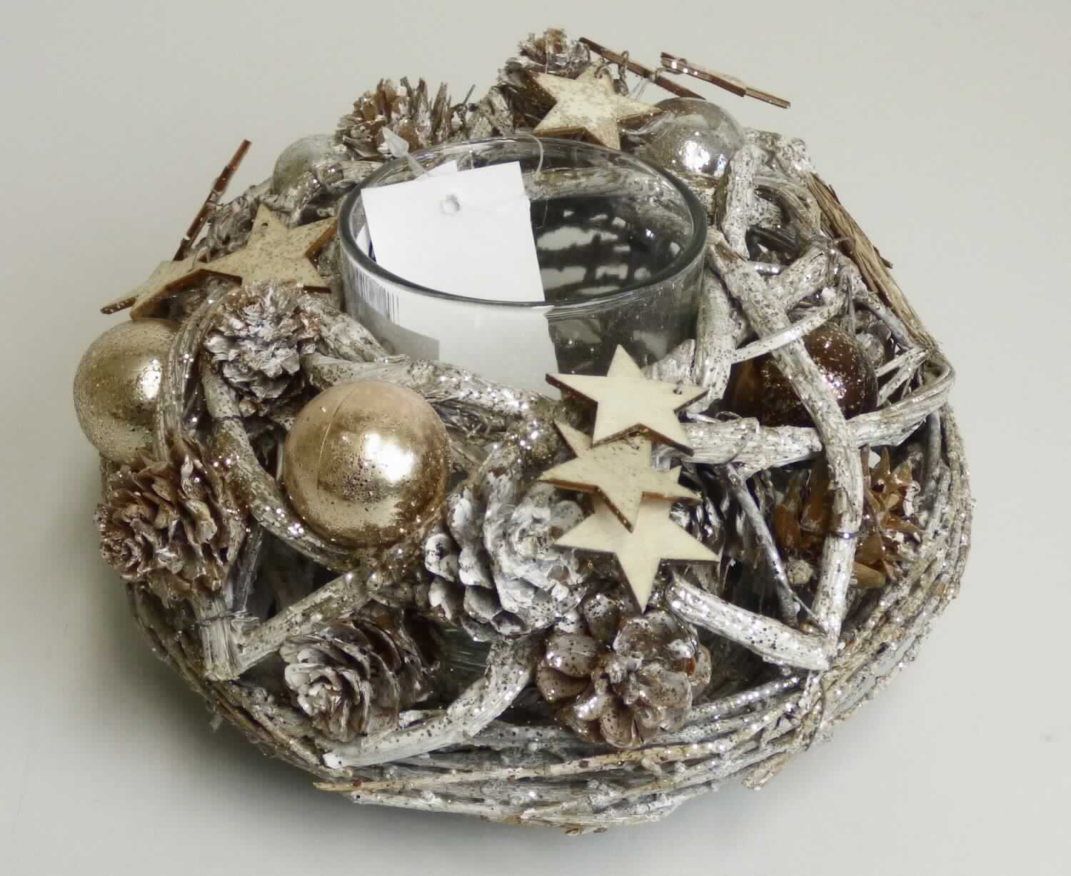 Nach den Antragsangaben sowie dem vorliegenden Warenmuster handelt es sich bei dem sog. "Kranz mit Teelicht silber/grau 17cm, Order 10258539" um eine runde, oben offene Halterung (Höhe ca. 10 cm), in die ein einfaches, klarsichtiges Glasgefäß (Durchmesser ca. 6,5 cm; Höhe ca. 8 cm) passgenau eingestellt ist.
Der Halter besteht aus einem Metallgestell, welches annähernd blickdicht mit beglitterten pflanzlichen Stoffen (überwiegend biegsame dünne Zweige, kein Rattan oder Bambus; Flechtstoffe i. S.d. Anmerkung 1 zu Kapitel 46) in Flechttechnik umwunden ist. Die Flechtstoffe sind zusätzlich mit dünnem Draht befestigt. 
An der Außenseite sind einige kleine Holzsterne, natürliche Kiefernzapfen und silbergraue bzw. goldfarbene Kunststoffkugeln zur Verzierung angebracht.
Derartige Waren werden üblicherweise in der Winterzeit zur Dekoration verwendet.
Die pflanzlichen Flechtstoffe verleihen der Ware gemäß AV 3 b) auf Grund des Umfangs und der Bedeutung in Bezug auf die Verwendung der Ware den wesentlichen Charakter.
Hinweise auf eine Fertigung in Handarbeit haben sich nicht ergeben.

Zolltarifrechtlich handelt es sich um eine "Flechtstoffware, unmittelbar aus pflanzlichen Flechtstoffen hergestellt, nicht aus Bambus oder Rattan, keine Flaschenhülsen aus Stroh, nicht handgearbeitet".