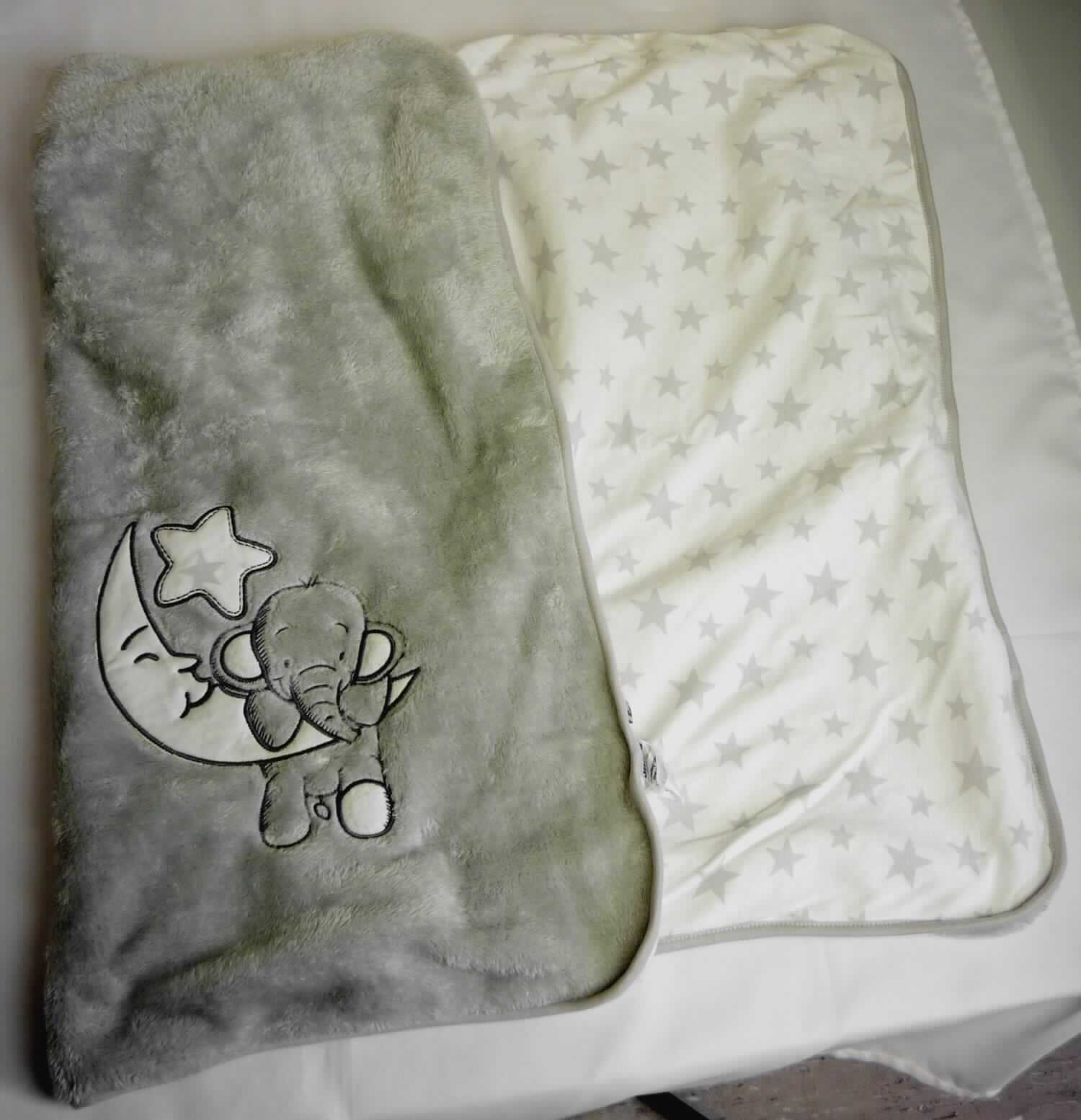 Decke, sog. Kuscheldecke Elephant, Foto siehe Anlage,
- in einem Polybeutel verpackt,
- annähernd rechteckig, mit abgerundeten Ecken; laut Antrag in den Abmessungen: 100 cm x 70 cm,
- zweilagig gearbeitet,
-- mit einer Außenseite (Schauseite) aus ca. 2,9 mm dicken, einfarbigen Plüschgewirken aus laut Antrag 
   100 % Polyester (synthetische Chemiefasern); mit einer Stickerei verziert,
-- mit einer Innenseite aus ca. 0,9 mm dicken, bedruckten Gewirken aus laut Antrag 100 % Baumwolle,
- ohne elektrische Heizvorrichtung,
- an allen Seiten mit einem schmalen Streifen aus glatten Gewirken eingefasst (somit konfektioniert),
- ohne Polsterung oder Füllung; somit keine Ware der Position 9404,
- ohne Beschaffenheitsmerkmale, die erkennen lassen, dass die Ware zur spielerischen Unterhaltung von Kindern 
  oder Erwachsenen dient; somit keine Ware der Position 9503,
- insbesondere im Hinblick auf die Bedeutung in Bezug auf die Verwendung als Kuscheldecke herrschen die 
  Plüschgewirke vor und bilden damit das für die Spinnstoffermittlung maßgebende Flächenerzeugnis.

"Decke, aus Spinnstoffen, ohne elektrische Heizvorrichtung, aus synthetischen Chemiefasern, aus Gewirken"