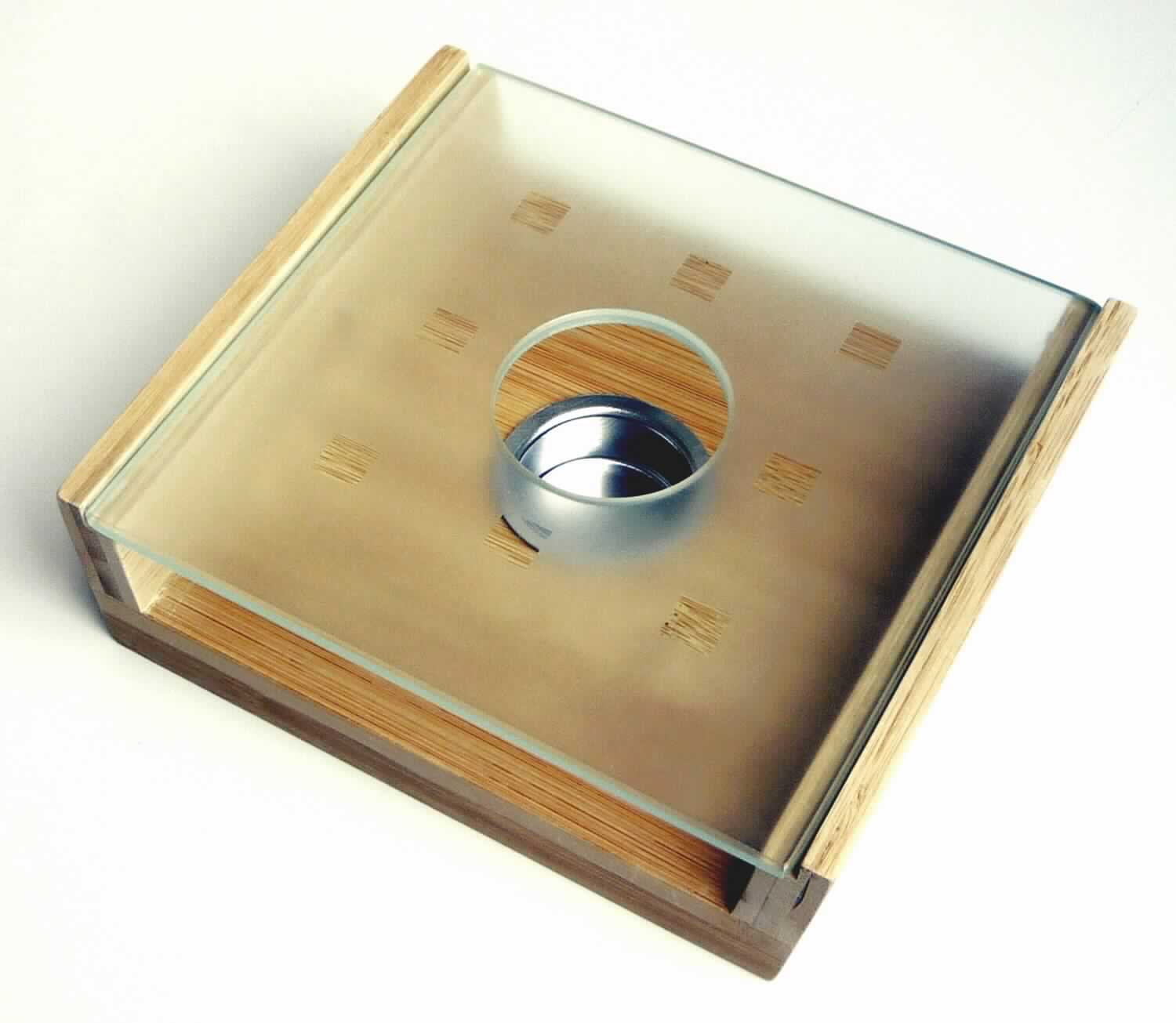 "Stövchen" (Abbildung siehe Anlage)
- rechteckiger Kasten mit 2 offenen Seiten (Abmessungen 18,0 x 16,0 x 5,5 cm) aus 
  aufeinander verleimten Lagen aus nebeneinander verleimten Bambusstreifen (Lagenholz), 
  im Boden mit einem eingesetzen Behälter aus unedlem Metall zur Aufnahme eines Teelichts, 
  oben mit einer in die zwei Seitenteile eingesetzten Platte aus Glas mit einer Öffnung zum 
  Einsetzen des Teelichts,
- zur Warmhalten von Speisen oder Getränken bei Tisch oder in der Küche.
Der Charakter der zusammengesetzten Ware wird aufgrund des Umfangs und des Wertes durch
das Holz bestimmt.

"Holzware zur Verwendung bei Tisch oder in der Küche, aus Bambus, kein Brotbrett, Schneidebrett 
 oder ähnliches Brett, keine Essstäbchen (zusammengesetzte Ware aus Holz - charakterbestimmend -,
 unedlem Metall und Glas) - sog. Stövchen"