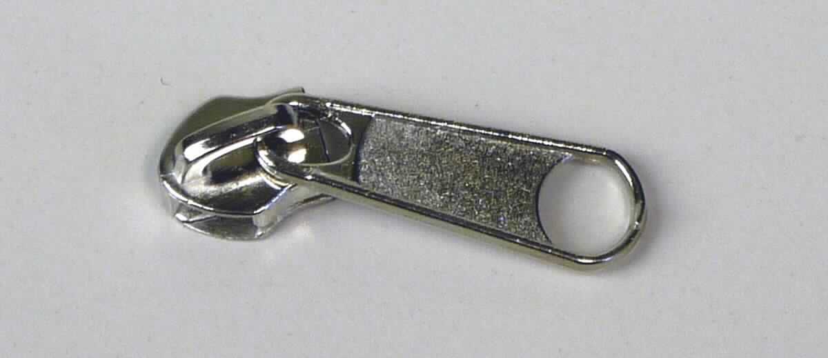 Bei dem sog. "Reißverschlußschlitten aus Nickel" handelt es sich um einen ca. 4 cm langen Schieber für Reißverschlüsse.  

Die Ware ist mit einem Griff ausgestattet, vollständig aus unedlem Metall  hergestellt, mit zwei schienenförmigen Aussparungen versehen und dient dazu, dass die Zähne eines Reißverschlusses ineinander verhakt und wieder gelöst werden können. 

Das Erzeugnis ist als erkennbares "Teil eines Reißverschlusses, aus unedlem Metall, Schieber" einzureihen.

Anlage: 1 Abbildung