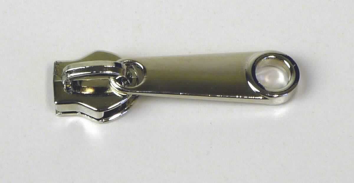 Bei dem sog. "Reißverschlußschlitten aus Nickel ohne Schloßloch" handelt es sich um einen ca. 4 cm langen Schieber für Reißverschlüsse.  

Die Ware ist mit einem Griff ausgestattet, vollständig aus unedlem Metall  hergestellt, mit zwei schienenförmigen Aussparungen versehen und dient dazu, dass die Zähne eines Reißverschlusses ineinander verhakt und wieder gelöst werden können. 

Das Erzeugnis ist als erkennbares "Teil eines Reißverschlusses, aus unedlem Metall, Schieber" einzureihen.

Anlage: 1 Abbildung