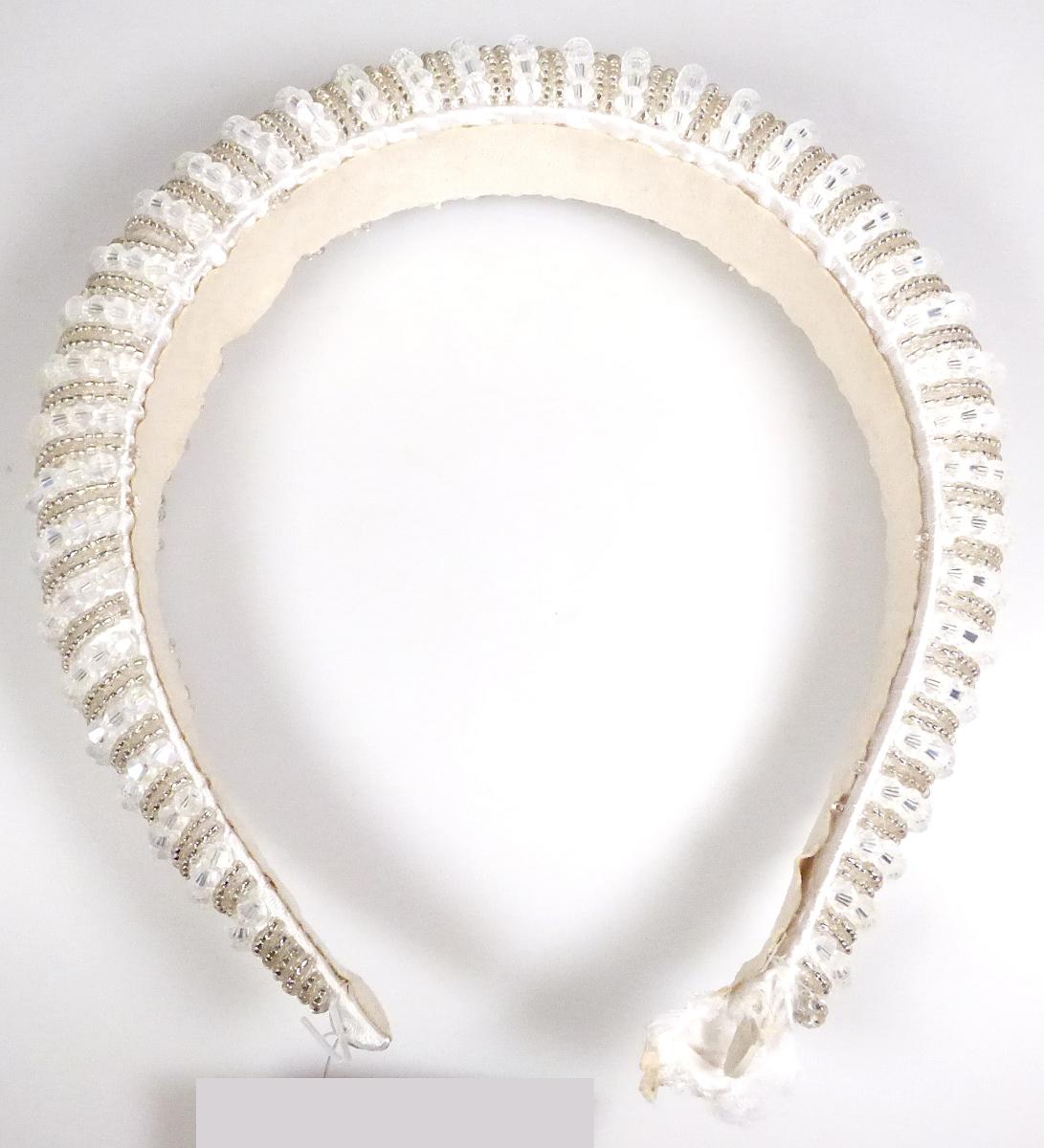 Bei der als "99-E047 - Haarreif mit Perlen" bezeichneten Ware handelt es sich um eine aus verschiedenen Stoffen zusammengesetzte Ware, bestehend aus einem ca. 3 cm breiten, gebogenen, der Kopfform angepassten, an den Enden offenen Reif aus Kunststoff, einer Polsterung aus Schaumkunststoff und einer äußeren Lage aus weißem Spinnstoff. Der Reif ist auf der Oberseite vollständig mit aufgefädelten Perlen aus Kunststoff bestückt. 

Der Haarreif wird zum Zusammenhalten des Haares und zugleich als Schmuck verwendet.

Bei dem aus unterschiedlichen Stoffen bestehendem Haarreif wird der stoffliche Charakter der Ware vom Kunststoff (charakterverleihend in Hinblick auf die Verwendung und des äußeren Erscheinungsbildes) bestimmt. 

Die Ware ist als "haarspangenähnliche Ware, aus Kunststoff" einzureihen.