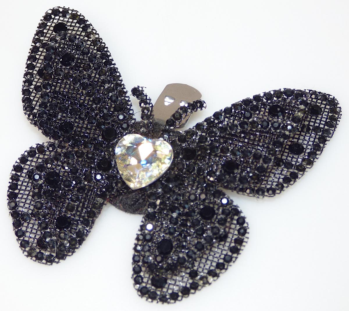 Bei dem Erzeugnis handelt es sich um einen stilisierten Schmetterling aus Spinnstoff (charakterbestimmend), der auf der Schauseite mit  verschieden großen Strasssteinchen aus Kunststoff verziert ist und auf der Rückseite mit einem Verschlussclip aus unedlem Metall zur Befestigung versehen ist. Das Erzeugnis dient der Verzierung von Schuhen, Hüten, Taschen, Kleidern und dergleichen und ist zu jeweils 2 Stück auf einer 10 cm x 15 cm großen Pappkarte für den Einzelverkauf aufgebracht.
Abmessungen: 5 cm x 6 cm
-Antragstellerangaben-

Abbildung siehe Anlage.

Derartige Erzeugnisse gehören als "anderer Fantasieschmuck, nicht aus unedlen Metallen" zum TARIC-Code 7117 9000 00.