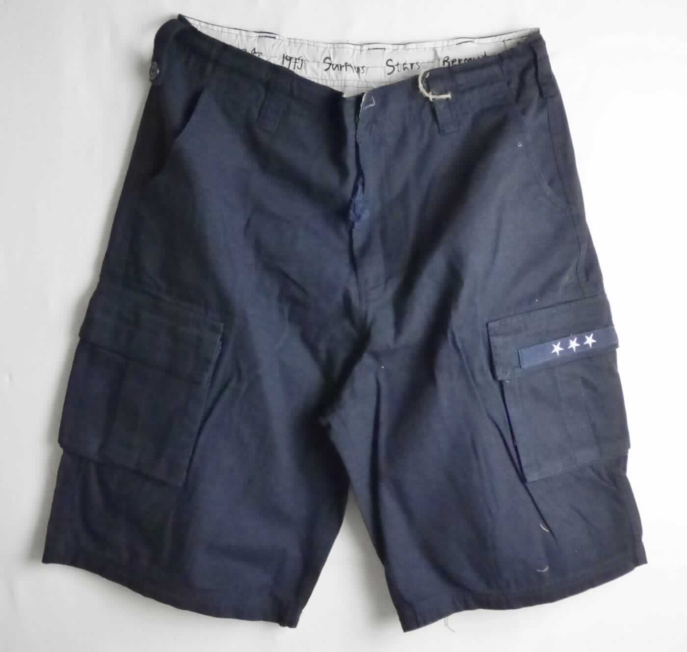 Kurze Hose, sog. Kurze Hose Surplus Stars Bermuda, Art. 07-5615-20, Größe L, Foto siehe Anlage,
- in einem Polybeutel verpackt,
- aus ca. 0,7 mm dicken, einfarbigen Geweben aus laut Antrag 100 % Baumwolle,
- in der Taille abschließend, mit einem ca. 4,5 cm breiten, angesetzten Taillenbund mit Gürtelschlaufen,
- vorn mit einer Öffnung mit Reißverschluss und Patte von links über rechts (Männerkleidung), die im Bund mit 
  einem Knopf geschlossen wird, 
- mit verschiedenen ein- und aufgesetzten Taschen,
- mit kurzen Hosenbeinen, die nicht die Knie bedecken (Seitenlänge: ca. 61 cm),
- an den Beinabschlüssen durch Umschlagen und Festnähen gesäumt.

"Kurze Hose, aus Geweben, für Männer, aus Baumwolle"