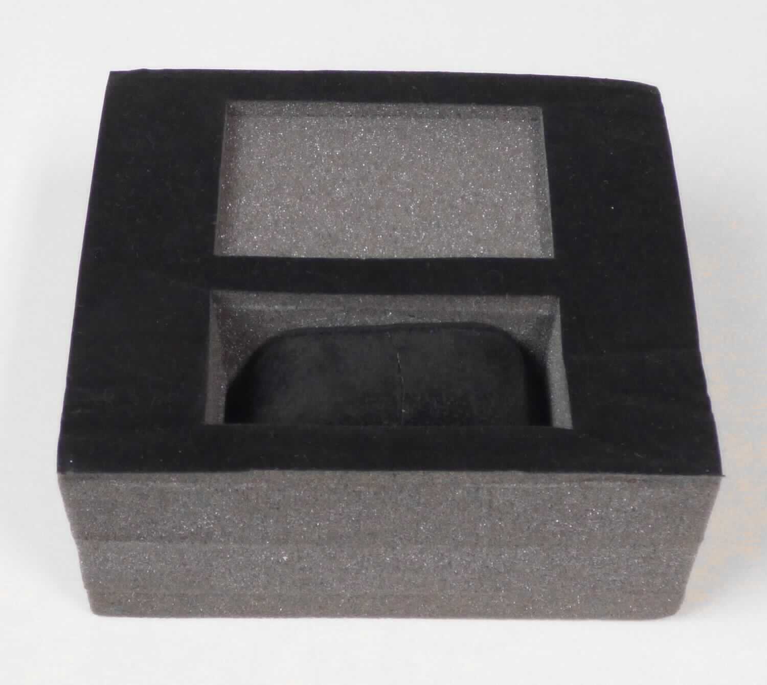 Bei dem als Warenmuster vorgelegten Erzeugnis handelt sich um eine Verpackungseinlage (sog. Schaumstoff-
einlage für Armbanduhren) in Form eines rechteckigen Blockes (Abmessungen (L x B x H) ca. 15,1 x 13 x 7 cm),
der aus vier zusammengeklebten Platten aus offensichtlich geschäumtem Kunststoff im Sinne der Anmerkung 1 
zu Kapitel 39 besteht. Der Block ist auf der Oberseite mit zwei unterschiedlich tiefen Aussparungen versehen. 
Die tiefere Aussparung ist mit einem speziell geformten Uhrenkissen ausgestattet, das herausnehmbar ist. Der 
Block ist um die Aussparungen herum mit einem Vlies aus Spinnstoff beklebt, das mit Scherstaub beflockt ist, 
so dass eine samtartige Oberfläche entsteht. Das eingelegte Uhrenkissen dient zur Befestigung einer Armbanduhr und besteht aus einem Kern aus Pappe, der mit Schaumkunststoff ummantelt und mit einem Gewebe überzogen 
ist, das ebenfalls mit Scherstaub beflockt ist. Eine Einreihung in die Position 3920 oder 3921 scheidet aus, da 
das Erzeugnis weiter bearbeitet ist als in der Anmerkung 10 zu Kapitel 39 zugelassen. 
Insbesondere im Hinblick auf den Umfang verleiht der Kunststoff der Verpackungseinlage ihren Charakter.

Derartige Erzeugnisse werden zolltarifrechtlich als "andere Transport- oder Verpackungsmittel aus Kunststoff, 
andere als in den TARIC-Codes 3923 1010 00 bis 3923 5090 00 genannt" eingereiht.