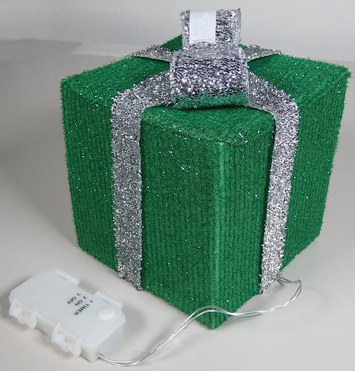 Dekorationsartikel, Foto siehe Anlage,
- in Form einer stilisierten Geschenkbox mit Schleife gearbeitet, in den Abmessungen (L x B x H) 
  von ca. 15 cm x 15 cm x 15 cm (ohne "Schleife"),
- mit einem formgebenden Gestell aus augenscheinlich Kunststoff, das auf der Außenseite mit 
  Ausnahme der Unterseite vollständig mit Gewirken (u. a. aus Chenillegarnen mit glänzenden 
  Streifen aus Spinnmasse) überzogen ist,
- mit einem umgebundenen "Geschenkband" und einer "Schleife" aus Gewirken (u. a. aus 
  metallisierten Streifen aus Spinnmasse); die doppelt gearbeitete "Schleife" ist auf der Unterseite 
  mit einem Zuschnitt aus Festkunststoff verstärkt und mittig mittels einer Niete aus unedlem 
  Metall mit dem Band fixiert,
- alle textilen Flächenerzeugnisse bestehen aus Spinnstoffen,
- mit einer im Inneren angebrachten, elektrischen Lichterkette mit mehreren laut Antrag LED-
  Brennstellen und einem Batteriefach (ohne Batterien) mit Timer-/An-/Aus-Druckschalter 
  ausgestattet; die Lichterkette dient lediglich der Erhöhung der Zierwirkung, somit keine Ware 
  der Position 9405,
- durch Zusammenfügen konfektioniert,
- keine Ware zur Innenausstattung der Position 6304, da ohne raumbezogene Funktion,
- erfüllt nicht die Bedingungen zur Einreihung als Festartikel in die Position 9505,
- aufgrund der verwendeten Flächenerzeugnisse keine Ware der Unterposition (KN) 6307 9098,
- insbesondere im Hinblick auf den Umfang und den Gesamteindruck bestimmen die Gewirke 
  aus Spinnstoffen gegenüber dem Kunststoff den wesentlichen Charakter der Ware.

"Andere konfektionierte Ware (Dekorationsartikel) aus Spinnstoffen, aus Gewirken"