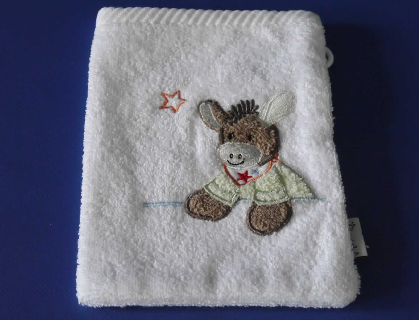 Es handelt sich um ein Set, bestehend aus sieben in einem Karton verpackten Waren: eine Wickelauflage, ein Kapuzenbadetuch, vier Waschlappen, ein Bade-Thermometer, ein Mittelmeerschwamm (Naturschwamm), ein Baby-Kamm und eine Baby-Bürste.  
Die Waren dienen weder der Befriedigung eines speziellen Bedarfs noch der Ausübung einer bestimmten
Tätigkeit und stellen sich somit nicht als Warenzusammenstellung i. S. d. AV 3 b) dar. Sie sind getrennt einzureihen.

Bei dem sog. Waschlappen, Art-Nr. 20441 0001 BS handelt es sich um einen Waschhandschuh
- aus ca. 3 mm dicken, weißen Schlingengeweben (Frottierware) aus 100 % Baumwolle,
- in den Abmessungen: 20 cm x 15 cm,
- an den Längsseiten und einer Schmalseite zusammengenäht, an der offenen Schmalseite 
  durch Umschlagen und Festnähen gesäumt und mit einer Aufhängeschlaufe 
  ausgestattet (somit konfektioniert),
- auf der Schauseite mit einer Stickerei (einen Esel darstellend) verziert,
- wird üblicherweise gewaschen,
- als Viererset in einer transparenten Kunststofftüte verpackt.

Die Ware ist als "Wäsche zur Körperpflege, aus Spinnstoffen, aus Frottierware aus Baumwolle, aus Geweben" einzureihen.