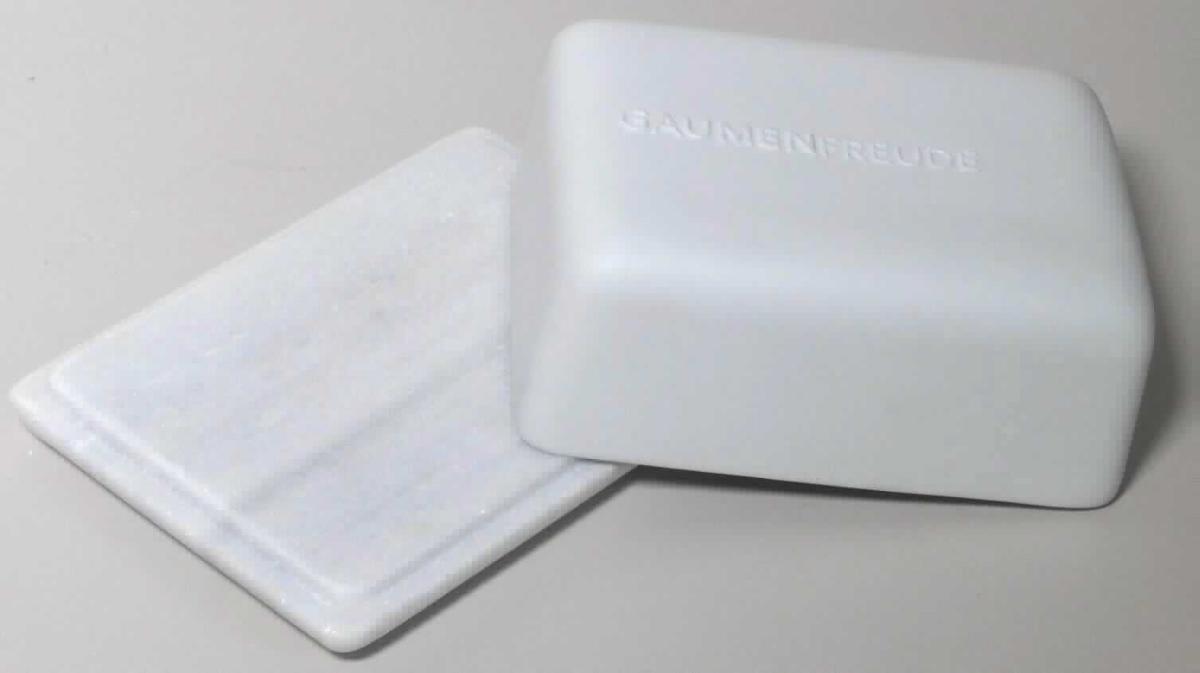 Angaben:
Butterdose mit Marmorplatte und passendem Porzellandeckel (außen unglasiert, innen glasiert) mit Prägung auf der oberen Schauseite; Abmessungen: Platte: 14 x 11 cm, Deckel: 12 x 9 x 5 cm.

Warenbeschaffenheit:
Weiß-graue, marmorierte, glatte Steinplatte mit Vertiefung am Rand, mit weißem, innen glasiertem, außen unglasiertem Deckel mit der Prägung "Gaumenfreude".

Befund:
Bearbeitete Werksteine und Waren daraus.

Zusammengesetzte Ware, bei der im Sinne der AV 3b) die Marmorplatte im Hinblick auf den Wert als charakterbestimmend angesehen werden.
