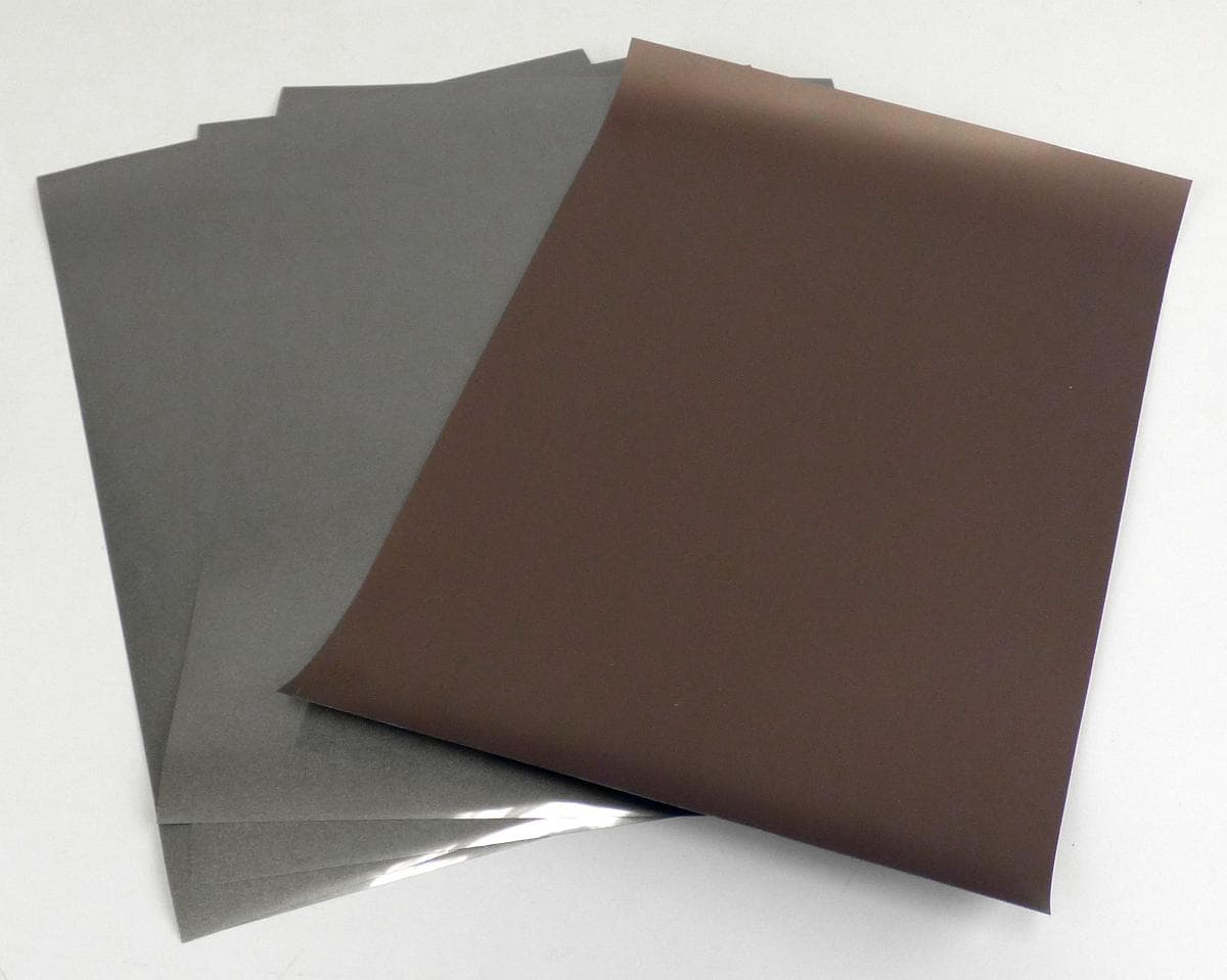 Angaben des Antragstellers:
Bei der Ware handelt es sich um eine reflektierende, farbige Transferfolie bestehend aus Mikroglasperlen, die mit einem hitzeaktivierten Klebstoff verbunden sind und eine transparente PET-Auskleidung aufweisen.

Feststellung an einem Warenmuster:
Es wurden fünf DIN A4 Bögen einer grau-braunen, schimmernden Folie mit transparenter, einseitig selbstklebender Schutzfolie vorgelegt. Die glitzernde Transferfolie besteht aus einer Polyester-Lage mit eingebetteten Glaskugeln.

Befund:
Es handelt sich um andere Folien, nicht aus Zellkunststoffen, weder verstärkt noch geschichtet (laminiert) oder auf ähnliche Weise mit anderen Stoffen verbunden, ohne Unterlage, aus anderen Polyestern.