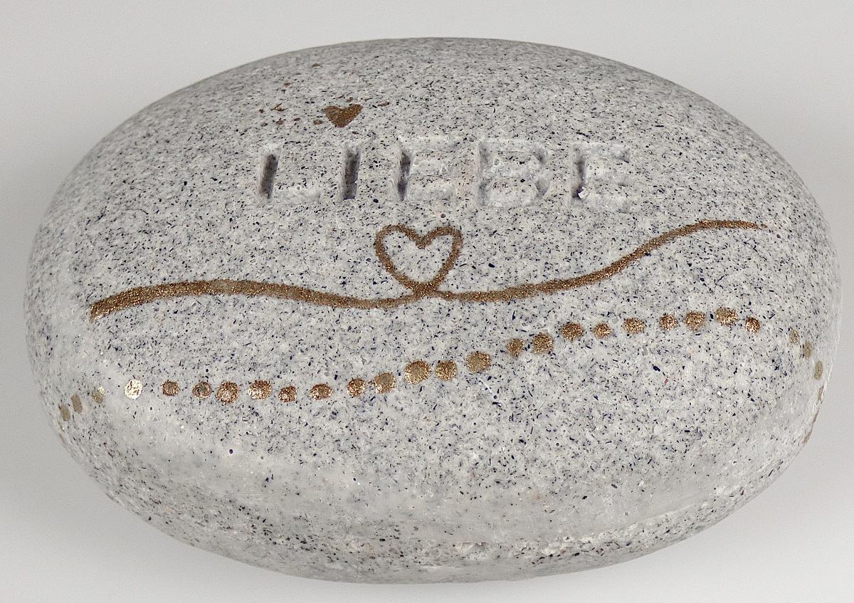 Angaben:
Waren aus Kunststein; Form: Steinform/Kieselsteinform; Dekor: mit eingeprägtem Schriftzug "Liebe" und Dekor in Goldlack; Funktion: als Geschenk- und Dekorationsartikel; Größe: ca. 6,5 cm x 5 cm x 2,5 cm.

Warenbeschreibung:
Grauer, ovaler, flacher, verzierter Stein (Abmessungen: ca. 7 x 5 x 3 cm), mit unterschiedlich großen Einschlüssen durchzogen, in Kieselstein-Optik.

Befund:
Waren aus Kunststein.