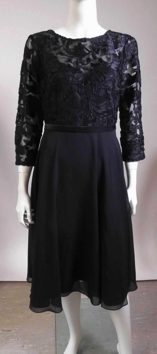 Kleid, sog. Kleid für Frauen, Style 7161100557, Größe 38, Foto siehe Anlage,
- im Bereich des Oberkörpers aus bis zu ca. 1 mm dicken, musterbildend in Ausbrennertechnik bedruckten 
  Gewirken und einem Rockteil aus ca. 0,5 mm dicken, einfarbigen Geweben,
- alle Flächenerzeugnisse aus laut Antrag synthetischen Chemiefasern,
- im Vorder- und im Rockteil gefüttert,
- über die Knie reichend (Rückenlänge: ca. 105 cm), 
- mit einem sog. U-Boot-förmigen Ausschnitt, 
- hinten mit einer teilweisen, bis in das Rockteil hineinreichenden Öffnung mit Reißverschluss und einem 
  am oberen Rand befindlichen Haken- und Ösenverschluss,
- mit 3/4-langen Ärmeln,  
- im Bereich der Taille mit einem stellenweise aufgenähten, ca. 2 cm breiten, umlaufenden "Band" aus Geweben 
  aus Spinnstoffen verziert,
- am unteren Rand durch Umschlagen und Festnähen gesäumt, 
- kann ohne ein weiteres den Unterkörper bedeckendes Kleidungsstück getragen werden,
- im Hinblick auf das äußere Erscheinungsbild sind die Gewirke als charakterverleihend anzusehen, im Hinblick auf 
  den Umfang und den Wert bestimmen jedoch die Gewebe den Charakter der Ware.

"Kleid, aus Geweben, für Frauen, aus synthetischen Chemiefasern"