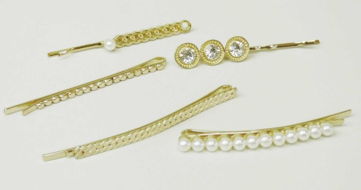 Bei dem sog. "Haarschieber, LAN 11581" handelt es sich um ein Set, bestehend aus fünf ca. 5 - 6,2 cm langen, u-förmig gebogenen Haarnadeln aus goldfarbigem Metall mit glatter Unterseite. Die obere Seite ist unterschiedlich gestaltet: mit drei geschliffenen, in runden Fassungen eingebetteten Glassteinen, mit aneinander gereihten Kunststoffperlen bzw. mit unterschiedlich geprägten Mustern im Ketten-Design.

Die Haarnadeln sind gemeinsam auf einer Kunststoffkarte mit Aufhängeöse in einer Kunststofftüte aufgemacht und werden zum Zusammen- bzw. Zurückhalten des Haares sowie als Haarschmuck verwendet.

Das Erzeugnis ist als "Haarnadel" einzureihen.