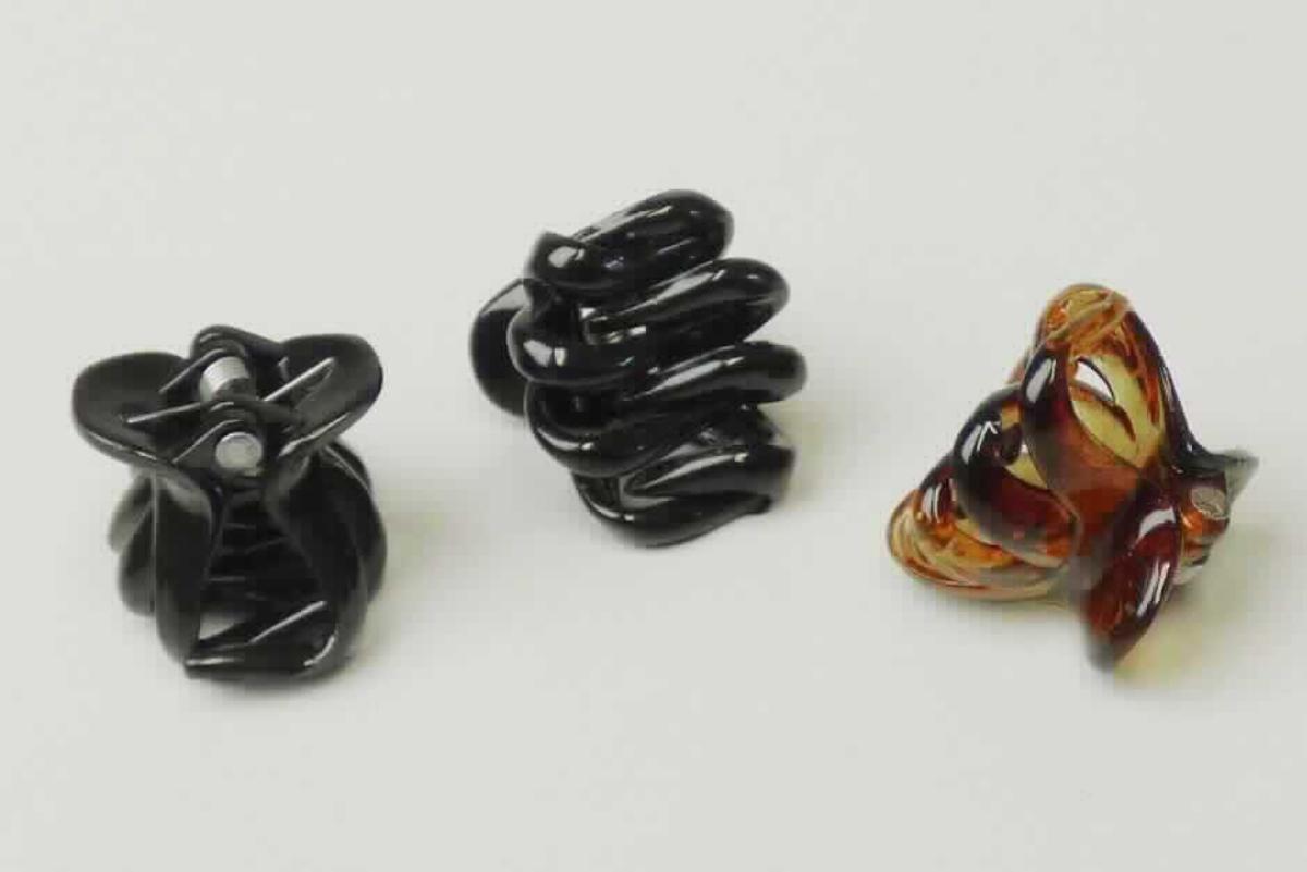 Bei der sog. "WWKs Octopus mini, LAN 11527" handelt es sich um vier Haarspangen mit einer Größe von ca. 2,5 x 1,9 x 1,7 cm (B x T x H) aus schwarzem bzw. braunem Kunststoff, bestehend aus zwei zueinander gebogenen Kämmen mit jeweils vier ineinandergreifenden Zinken. Mittels eines im Griffbereich befindlichen Stiftes, auf dem eine Feder fixiert ist, werden die Kämme zusammengehalten.

Mithilfe der Feder werden die Kämme auseinandergedrückt, sodass die aufgeklappten Spangen im Haar angesetzt werden können und anschließend nach dem Zusammenklappen im Haar fixiert sind.
Die Waren bestehen aus Kunststoff (charakterbestimmendes Material insbesondere aufgrund des Umfangs), lediglich die Feder und der Stift bestehen aus unedlen Metallen.
Das Erzeugnis dient dem Schmücken sowie dem Zusammenhalten der Haare.

Vier Haarspangen sind auf einer bedruckten Kunststoffkarte mit Aufhängeöse aufgemacht und als "Haarspange, aus Kunststoff" einzureihen.