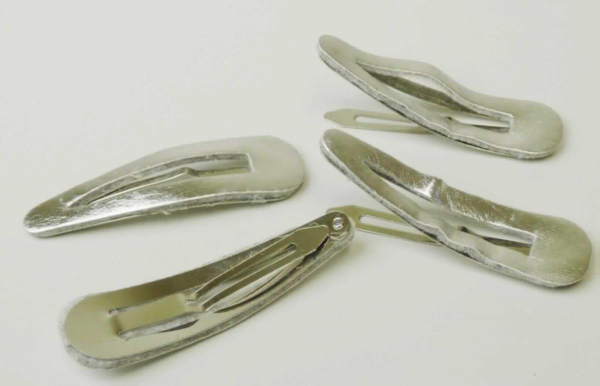 Bei der sog. "Schlafklammer, LAN 11573" handelt es sich um eine aus verschiedenen Stoffen zusammengesetzte Ware in Form eines Haarclips (Haarspange). Die Ware besteht aus einer auf Spannung gebogenen, ca. 6 x 1,7 cm großen Metallspange und einem passgenauen aufgeklebten, silberfarbenen Kunstleder mit darunter befindlichem Vliesstoff.

Der stoffliche Charakter wird durch das Metall aufgrund seiner Bedeutung für die Verwendung bestimmt. 

Das Erzeugnis dient dem Zusammenhalten des Haares und ist als Set zu je vier Spangen auf einem Pappaufhänger in einer Kunststofftüte aufgemacht. 

Die Ware ist als "Haarspangen aus unedlem Metall" einzureihen.