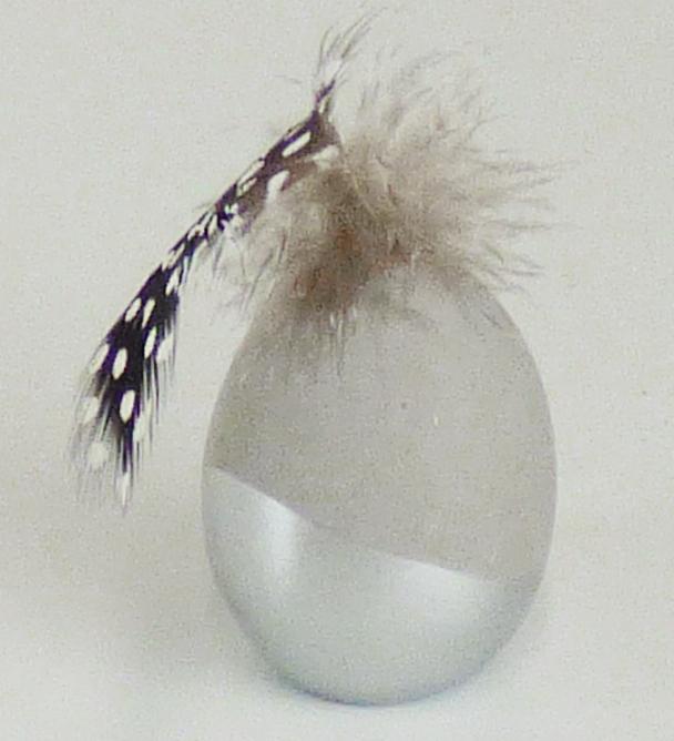 Angaben:
4er-Set Ostereier zum Hinstellen mit Feder; Material: Beton mit Perlhuhn-Feder.

Warenbeschaffenheit:
Graues Ei (Höhe ca. 6 cm; homogenes, graues Material) im unteren Bereich silberfarben bemalt, mit einer Feder verziert.

Befund:
Waren aus Zement, Beton oder Kunststein.
Zusammengesetzte Ware, bei der im Hinblick auf den Umfang und die Bedeutung für die Verwendung das Ei aus Beton als charakterbestimmend angesehen wird.