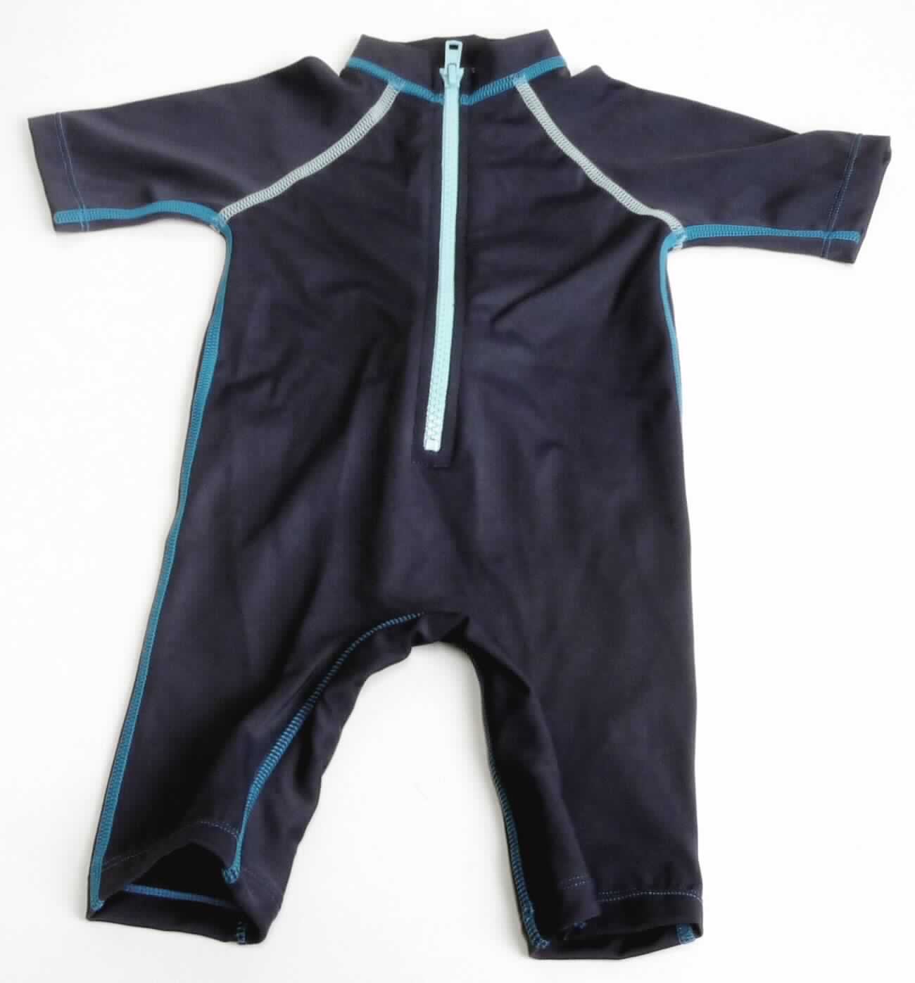 Kleidung für Kleinkinder, sog. Badeanzug, Art. 14310019113, Größe 6mo., Foto siehe Anlage,
- aus ca. 0,6 mm dicken, einfarbigen Gewirken aus laut Antrag 82 % Polyamid und 18 % Elasthan/Lycra (beides 
  synthetischen Chemiefasern),
- den Rumpf sowie Teile der Arme und Beine bedeckend,
- mit einem Stehkragen,
- vorn mit einer nicht durchgehenden Öffnung mit Reißverschluss, 
- im Bereich des Schritts und der Beininnenseiten mit einem eingenähten Schrittfutter in Art einer Hygieneeinlage,
- an den Beinabschlüssen durch Umschlagen und Festnähen gesäumt,
- aufgrund des verwendeten Flächenerzeugnisses keine Ware des Kapitels 62,
- aufgrund der Größe für Kinder unter 18 Monaten bestimmt, somit Kleidung für Kleinkinder.

"Kleidung, aus Gewirken, für Kleinkinder, aus synthetischen Chemiefasern"