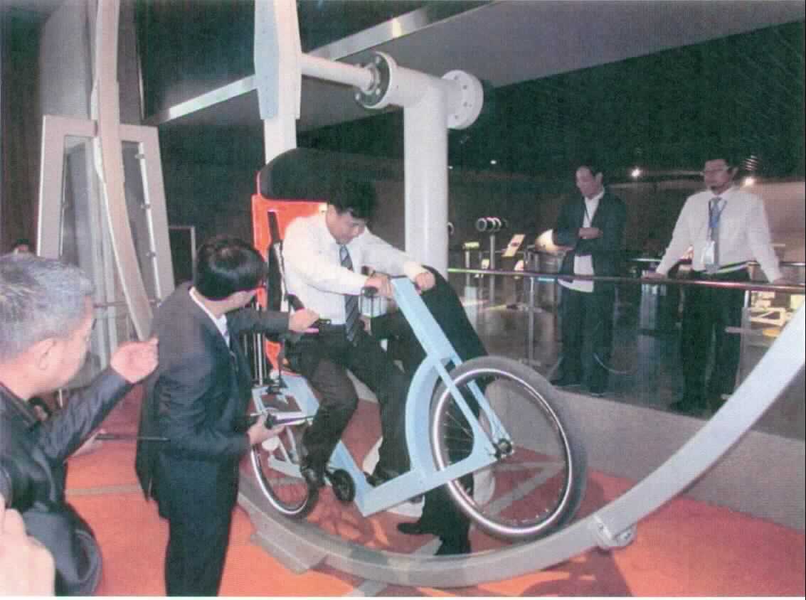 Bei dem Erzeugnis mit der Bezeichnung "360 Degree Bike" handelt es sich seiner Beschaffenheit und der vorgesehenen Verwendung nach um ein Exponat zu Vorführzwecken in Museen, Science Centern und ähnlichen Einrichtungen, das zur ausschließlichen Wissensvermittlung eines wissenschaftlichen Phänomens dient.

Das Exponat "360 Degree Bike", Seriennr.: 9468, zeigt experimentell die Wirkungsweise von kinetischen und Gravitations-Energiekräften. 

Der Besucher wird an einem Fahrrad mit festem Gang gesichert, das über einen Schwenkmechanismus an einer 360-Grad-Schlaufe befestigt ist. Er erfährt solchermaßen die Wechselwirkung von Beschleunigung und Gravitation.

Das ca. 2060 kg schwere Erzeugnis ist zur Interaktion durch den Betrachter / Besucher vorgesehen. 

Hauptbestandteile des Exponats (teilweise noch nicht zusammengesetzt):
- Baugrund,
- Stahlzaun,
- Stahlrahmen,
- Rotationsarm,
- 360-Grad-Bahn mit einem Durchmesser von 4920 mm,
- spezifiziertes Fahrrad und
- Steuerungskonsole, ggf. Schautafeln oder dergleichen.

Die Ware ist als "Instrument, Apparat, Gerät und Modell, seiner Beschaffenheit nach zu Vorführzwecken bestimmt, nicht zu anderer Verwendung geeignet, nicht von dem TARIC-Code 9023 0010 00 erfasst" einzureihen.

Anlage: 1 Abbildung