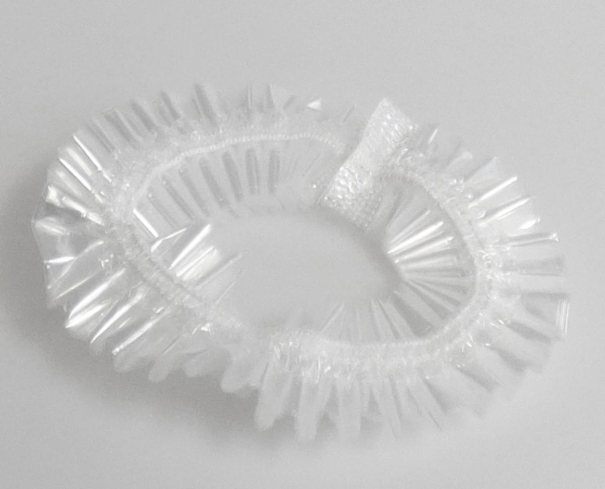 Kopfbedeckung, sog. Duschhaube, Foto siehe Anlage,
- aus einer klarsichtigen Kunststofffolie gearbeitet,
- der Kopfform annähernd angepasst hergestellt,
- am Rand mit einem elastischen Gummizug verengt und mit einem Faden aus Spinnstoffen gesäumt,
- zur Verwendung als Schutzhaube beim Duschen zum Bedecken des gesamten Haares,
- in einem kleinen, bedruckten Karton aus Pappe verpackt.

"Andere Kopfbedeckung (Duschhaube), aus Kunststoff"