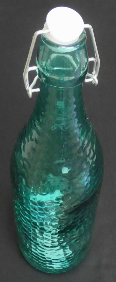 Flasche aus Glas, sog. Glasflasche mit Bügelverschluss, Artikel 19757, Foto siehe Anlage,
- aus gefärbtem (türkisfarbenem) Glas (nicht aus Glasröhren hergestellt); mit wabenartiger Struktur,
- mit einem Bügelverschluss aus unedlem Metall und einem Stopfen aus Kunststoff mit einem Dichtungsring,
- mit einem Fassungsvermögen (Nenninhalt) von 1000 ml,
- in den Abmessungen: ca. 8,5 cm (Durchmesser) x 30 cm (Höhe),
- zur Aufnahme von Nahrungsmitteln oder Getränken.

"Flasche aus Glas, zu Transport- oder Verpackungszwecken, nicht aus Glasröhren hergestellt, 
 aus gefärbtem Glas, mit einem Nenninhalt von 1 l, für Nahrungsmittel und Getränke"