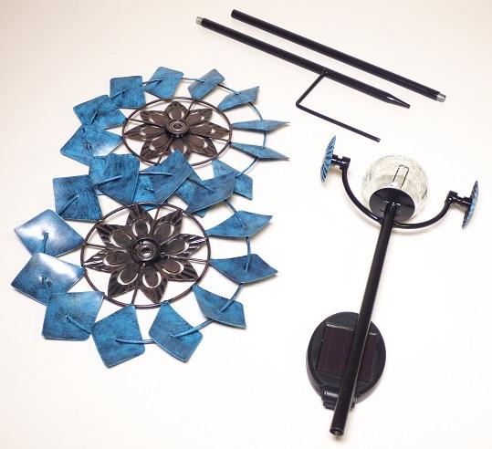 Sogenannte Solar Metall Windspinner Blume der Artikelnummern 9988176 und 9987777, nachfolgender Beschaffenheit:
Maße ca. 230x120x920 mm
Gewicht ca. 600g
Materialien:
Blume aus unedlem Metall
Kugel aus Glas
Solar Modul überwiegend aus Kunststoff

Ware in zwei verschiedenen Ausführungen:
blau
rosa
mit wiederaufladbaren Batterien 
Die Erzeugnisse sollen als Ziergegenstände in Gärten verwendet werden.
- Antragstellerangaben -

Abbildung siehe Anlage.

Das unedle Metall ist in Bezug auf die Bedeutung für die Verwendung (Formgebung) und nach Umfang gegenüber den anderen Materialien charakterbestimmend.
  
Derartige Erzeugnisse gehören als "andere Ziergegenstände aus unedlen Metallen, nicht versilbert, vergoldet oder platiniert" zur Codenummer 8306 2900 00 0.