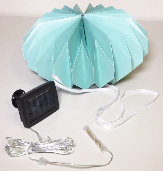 Bei dem sog. Solar Lampion grün, Artikelnummer 9987581 handelt es sich um einen noch nicht zusammengesetzten elektrischen Beleuchtungskörper aus grünem, lichtdurchlässigem Papier. Das ausfaltbare Gehäuse hat eine runde, bauchige Form mit zackigen Einschnitten (Durchmesser: ca. 30 cm, Höhe: ca. 15 cm) und dient als Lampenschirm. Zur Stabilisierung dienen zwei Ringe aus unedlem Metall sowie vier magnetische Kontakte. Die Beleuchtung erfolgt photovoltaisch mit einer im Gehäuse eingesetzten Lichterkette mit 10 Leuchtdioden, die durch ein ca. 3 m langes Kabel mit dem Photovoltaikmodul verbunden ist. Das Erzeugnis kann mittels einer ca. 1 m langen textilen Schnur aufgehängt werden und dient zu Beleuchtungszwecken in der Art eines Stimmungslichtes.

Hinweise auf eine Handfertigung liegen nicht vor.

Das Erzeugnis ist als „elektrischer Beleuchtungskörper, anderweit weder genannt noch inbegriffen, nicht von den Unterpositionen (HS) 9405 11 bis 9405 39 erfasst, photovoltaisch, ausschließlich zur Verwendung mit LED-Lichtquellen bestimmt, kein Scheinwerfer, aus Papier und Metall, nicht handgearbeitet“ einzureihen.