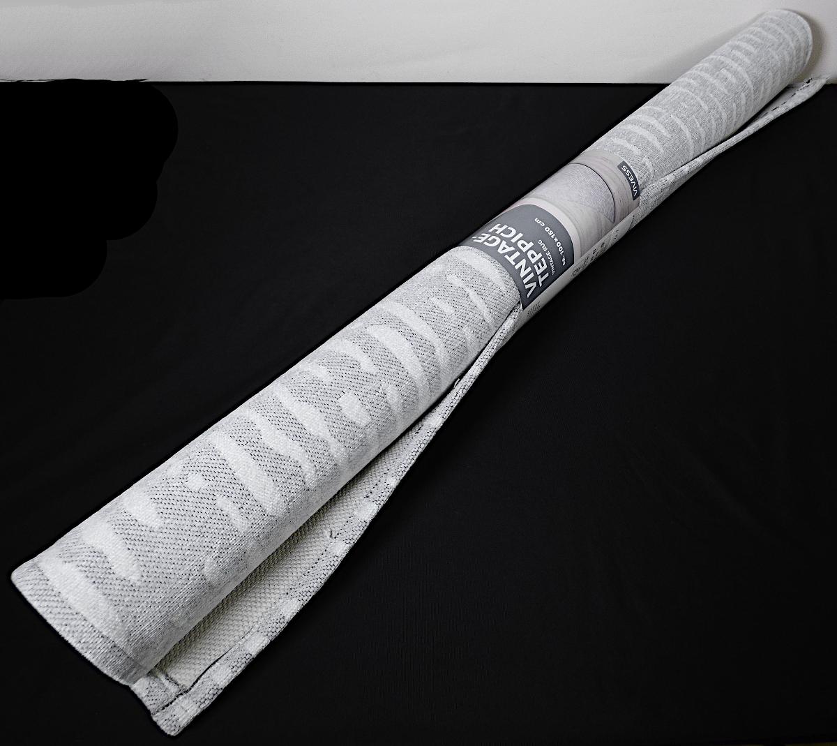 Teppich, sog. Vintage Teppich, Foto siehe Anlage,
- auf eine Papphülse gerollt und mit einer bedruckten Pappbanderole umwickelt,
- rechteckig, in den Abmessungen von laut Antrag ca. 100 cm x 150 cm,
- aus einem Gewebe, somit keine Ware der Position 5703,
- laut Antrag aus 54 GHT Polyester (synthetischer Spinnstoff) und 46 GHT Baumwolle,
- auf der Rückseite mit geprägtem Schaumkunststoff ausgerüstet,
- ohne Flor,
- kein Kelim, Sumak, Karamanie oder ähnlicher Teppich,
- weder getuftet noch beflockt,
- an den Rändern gesäumt (somit konfektioniert).

"Teppich aus synthetischen Spinnstoffen, gewebt, weder getuftet noch beflockt, konfektioniert, anderer
 als in der Unterposition 5702 10 genannte, ohne Flor, aus Polyester"