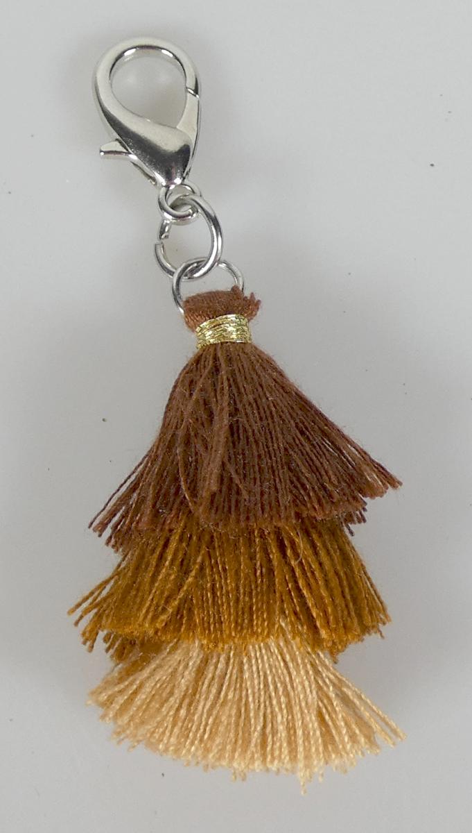 Es handelt sich um Anhänger für Schuhe, Kleidung oder ähnlichem, Bommel (Tassel) aus Garnen an einem kleinen Karabinerhaken aus unedlem Metall.
- Antragstellerangaben -
Der Anhänger besteht aus Bündeln von Spinnstoffgarnen, die in halber Länge umgelegt und unterhalb des Knickendes abgebunden sind (Troddeln im Sinne der Position 5808)
und die an einem Ring befestigt sind, der an einem zweiten Ring hängt, an dem wiederum ein Karabinerhaken hängt.
Ringe und Karabinerhaken bestehen aus unedlem Metall.
Gesamtlänge etwa 6 cm.
Abbildung siehe Anlage.
Derartige Erzeugnisse gehören als "anderer (als in den Unterpositionen 7117 1100 00 und 7117 1900 genannter) Fantasieschmuck (aus Spinnstoff und unedlem Metall)"
zum TARIC-Code 7117 9000 00.