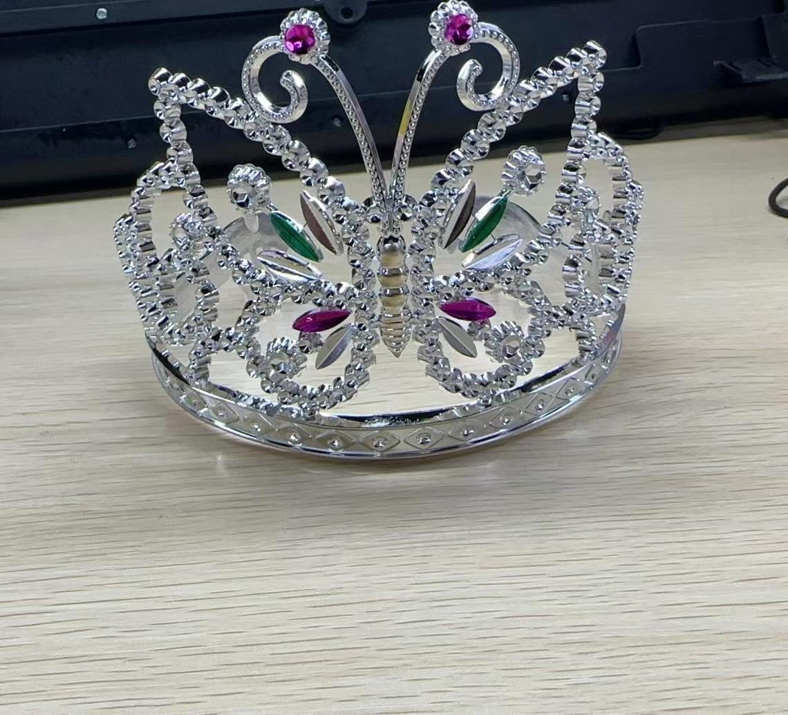 Sogenannte "Kronen - Diademe - aus Kunststoff" mit verzierenden Steinen aus Kunststoff, in sechs verschiedenen Ausfertigungen:

Es handelt sich bei den sogenannten "Kronen - Diademen - aus Kunststoff" um halboffene Reife zur Verzierung (als Kopfschmuck) in Form von Kronen, mit Durchbrechungen versehenen, die mit farbigen Steinen aus Kunststoff versehen sind.

Abbildung siehe Anlage.

Eine Einreihung in die Position 9615 kommt nicht in Betracht, weil die Ware weder zum Frisieren noch als Schmuck des Haares dient. Vielmehr handelt es sich um Kopfschmuck, der horizontal auf den Kopf gesetzt wird und der durch das aufgesetzte Zierelement den Kopf bzw. den Träger schmückt. Derartige Waren werden in eine bereits bestehende Frisur eingesteckt und z. B. mittels weiterer Haarspangen oder Haarnadeln befestigt. Eine Einreihung in das Kapitel 95 als Spielzeug oder Karnevals-/Faschingsartikel ist aufgrund des eigenständigen Gebrauchswertes des Diadems als Schmuckware ausgeschlossen.

Derartige Erzeugnisse gehören als "anderer Fantasieschmuck, nicht aus unedlem Metallen" zum TARIC-Code 7117 9000 00.