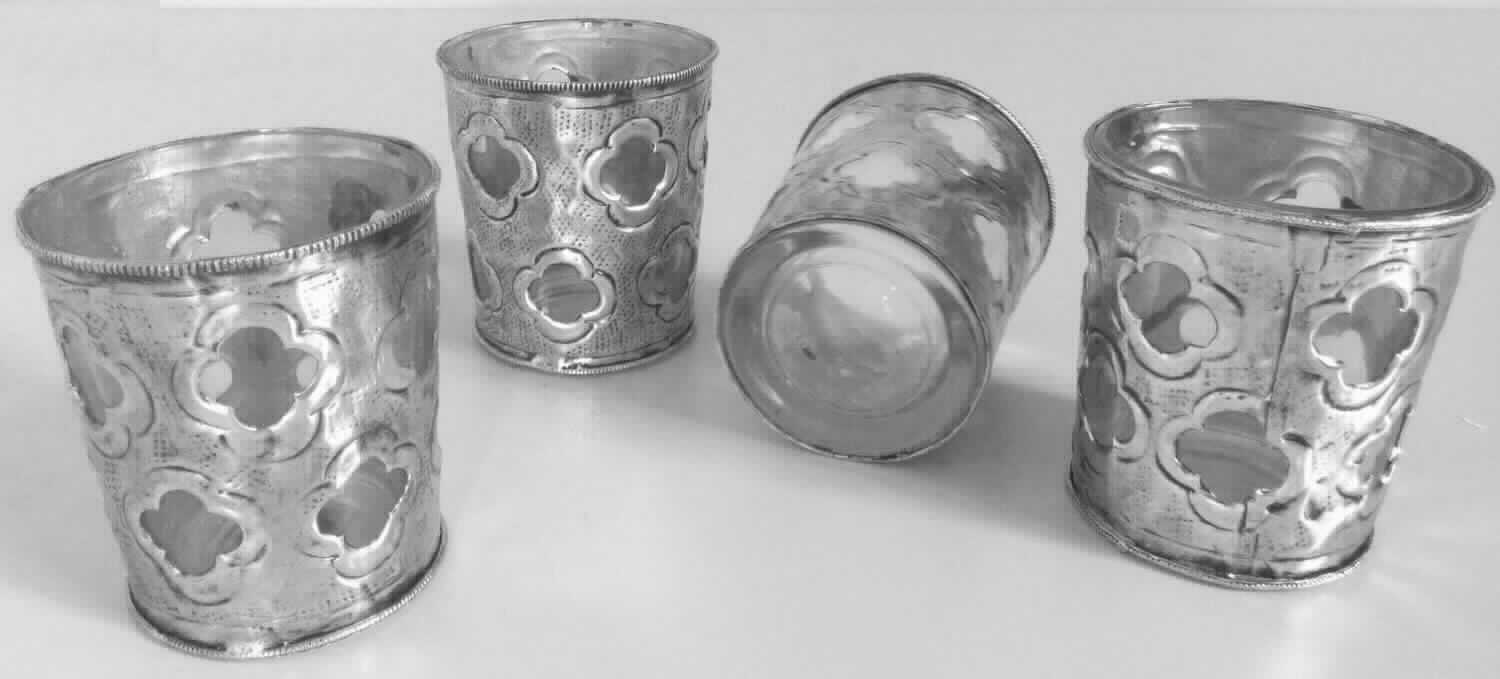 Glasware zur Innenausstattung, Foto siehe Anlage,
- als Set mit vier Stück,
- in Form einer zusammengesetzten Ware, bestehend aus:
- - einem becherartigen, oben offenen Gefäß aus klarsichtigem Glas; laut Antrag aus gewöhnlichem,
    handgefertigtem Glas (manuelle Glasentnahme),
- - - in den Abmessungen: ca. 7,5 cm (Höhe) x 6,7 cm (max. Durchmesser),
- - ornamentartigen Verzierungen an der Außenseite des Glasgefäßes,
- - - aus unedlem Metall (laut Antrag Eisen),
-  der Wert des Glases und des unedlen Metalls ist laut Antrag genau gleich; das Glas bestimmt im Hinblick auf den
   Umfang und die Verwendung der Ware als Windlicht den Charakter der zusammengesetzten Ware, daher keine
   Einreihung als Ziergegenstand aus unedlem Metall in die Position 8306,
- keine Einreihung als nicht elektrischer Beleuchtungskörper in die Position 9405, da die Gefäße weder eine
  Haltevorrichtung, noch eine spezifische Vorrichtung zum Befestigen einer Kerze oder eines Teelichtes aufweisen,
- verpackt in einem Pappkarton mit einem Einleger aus Styropor.

"Glasware zur Innenausstattung, aus gewöhnlichem Glas, handgefertigt"