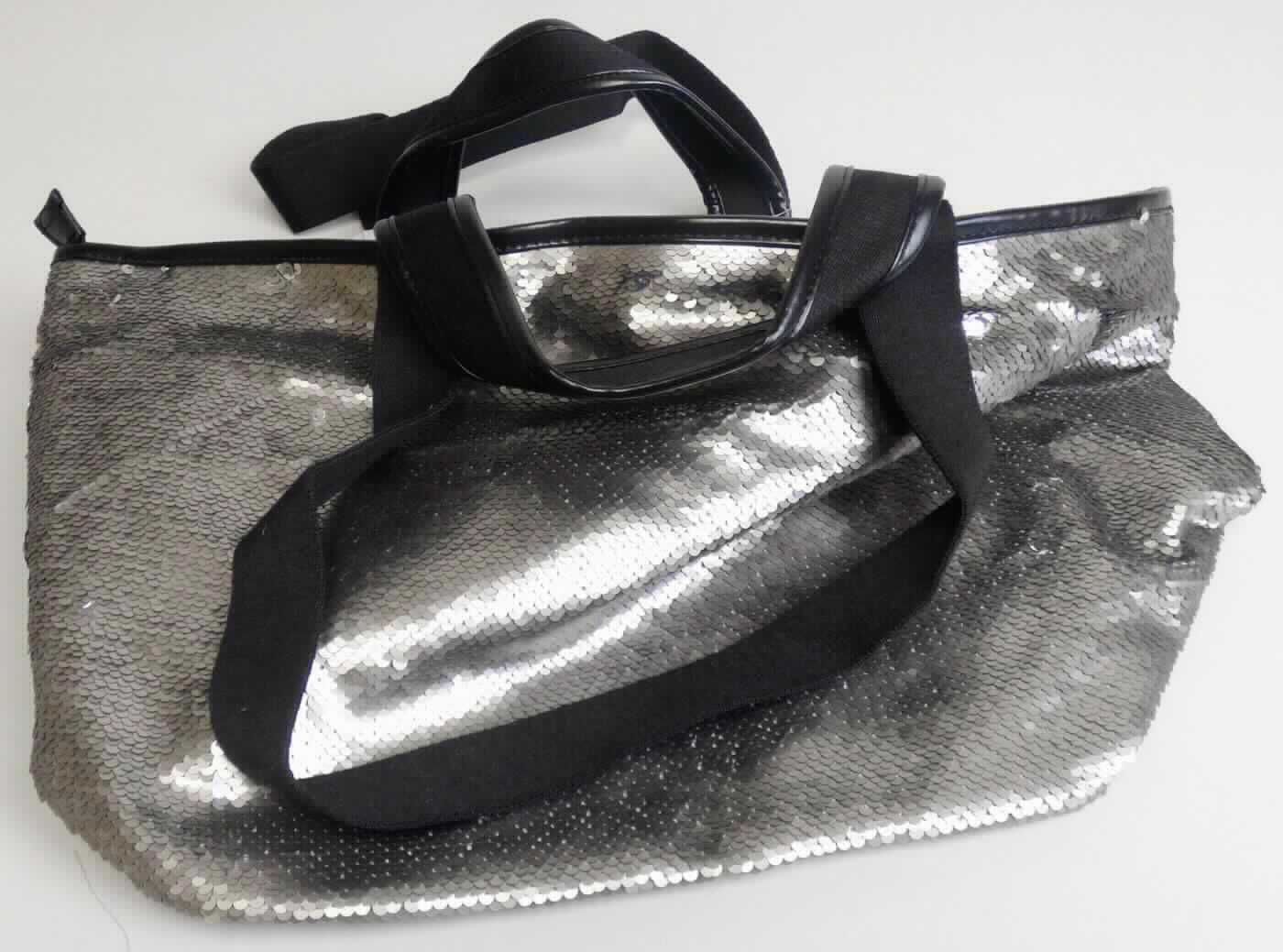 Ähnliches Behältnis (Umhängetasche), sog. Tasche matt gold Pailletten, Foto siehe Anlage,
- mit einer Außenseiten aus mit Pailletten bestickten Geweben aus Spinnstoffen der Position 5810 (Applikations-
  stickerei), wobei die Pailletten aus Kunststoff das Gewebe aus Spinnstoffen bedecken und den mit bloßem Auge
  wahrnehmbaren Stoff an der Oberfläche bilden; lediglich am oberen Rand der Tasche mit einer Randeinfassung 
  mit einer Außenseite aus Kunststofffolien,
- mit zwei Handtragegriffen und zwei Schultertragegurten,
- mit einem ca. 4 cm unterhalb des oberen Rands verlaufenden Reißverschluss,
- gefüttert und mit einem Reißverschlussfach sowie zwei offenen Einsteckfächern ausgestattet,
- in den Abmessungen: ca. 52 cm (max. Breite) x 29 cm (Höhe) x 26 cm (Tiefe).

"Ähnliches Behältnis, anderes als in den Unterpositionen 4202 1110 bis 4202 3900 genannte, mit einer anderen
 Außenseite als in den Unterpositionen 4202 9110 bis 4202 9298 genannte, kein handgearbeitetes Behältnis für
 Musikinstrumente"