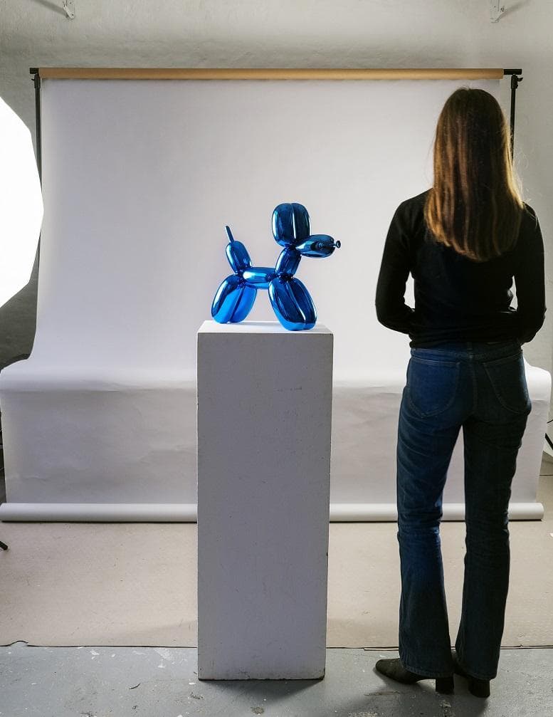 Bei der durch Abbildungen und Angaben des Anmelders veranschaulichten Ware handelt es sich um eine Skulptur mit dem Titel „Balloon Dog/Blue“ aus Porzellan in Form eines freistehenden Hundes, mit einer glänzenden, blauen, metallisierten Oberfläche (Größe ca. 40 x 48 x 15,8 cm). Das verfremdet dargestellte, scheinbar aus Luftballons geformte Tier wurde im Jahr 2021 unter der Anleitung des Künstlers Jeff Koons in Zusammenarbeit mit der renommierten Porzellan-Manufaktur "Bernardaud" (Limoges; Frankreich) aus Limoges-Porzellan gefertigt. Es handelt sich um eine verkleinerte Nachbildung der von dem Künstler im Rahmen der Celebration-Serie (1994-2000) geschaffenen weltbekannten Großskulpturen.
Die Urheberschaft des Künstlers wird durch eine vorhandene Signatur an der Innenseite des rechten Vorderbeins der Tierfigur belegt. Die Arbeit besitzt keinen handelsgängigen Charakter.
Die Skulptur ist als "Originalerzeugnisse der Bildhauerkunst, aus Stoffen aller Art, weniger als 100 Jahre alt"  einzureihen.