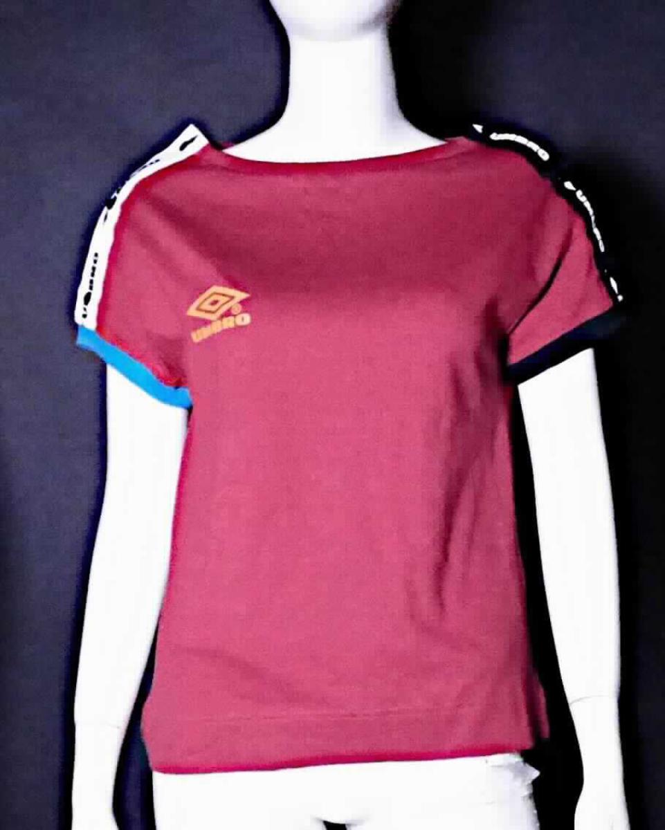 Bluse, sog. UMBRO LINA POPPER TEE Women, Größe XS, Foto siehe Anlage,
- in einem Polybeutel verpackt,
- aus ca. 0,5 mm dicken, einfarbigen Gewirken aus laut Antrag 100 % Baumwolle, mit durchschnittlich mehr als
  10 Maschen je linearen Zentimeter in jeder Richtung,
- über die Taille reichend (Rückenlänge: ca. 58 cm),
- mit einem runden Halsausschnitt mit gerippt gewirkter Randeinfassung,
- auf beiden Schultern mit einer bis zu den Ärmelenden reichenden Öffnung mit Druckknopfverschluss (somit 
  kein T-Shirt oder modisches Unterhemd),
- ohne Hinweise auf den Trägerkreis (unisex),
- mit kurzen Ärmeln; mit gerippt gewirkten Bündchen an den Ärmelenden,
- vorn und an den Ärmeln mit Motiv und Schriftzug bedruckt,
- am unteren Rand durch Umschlagen und Festnähen gesäumt.

"Bluse, aus Gewirken, für Frauen, aus Baumwolle"