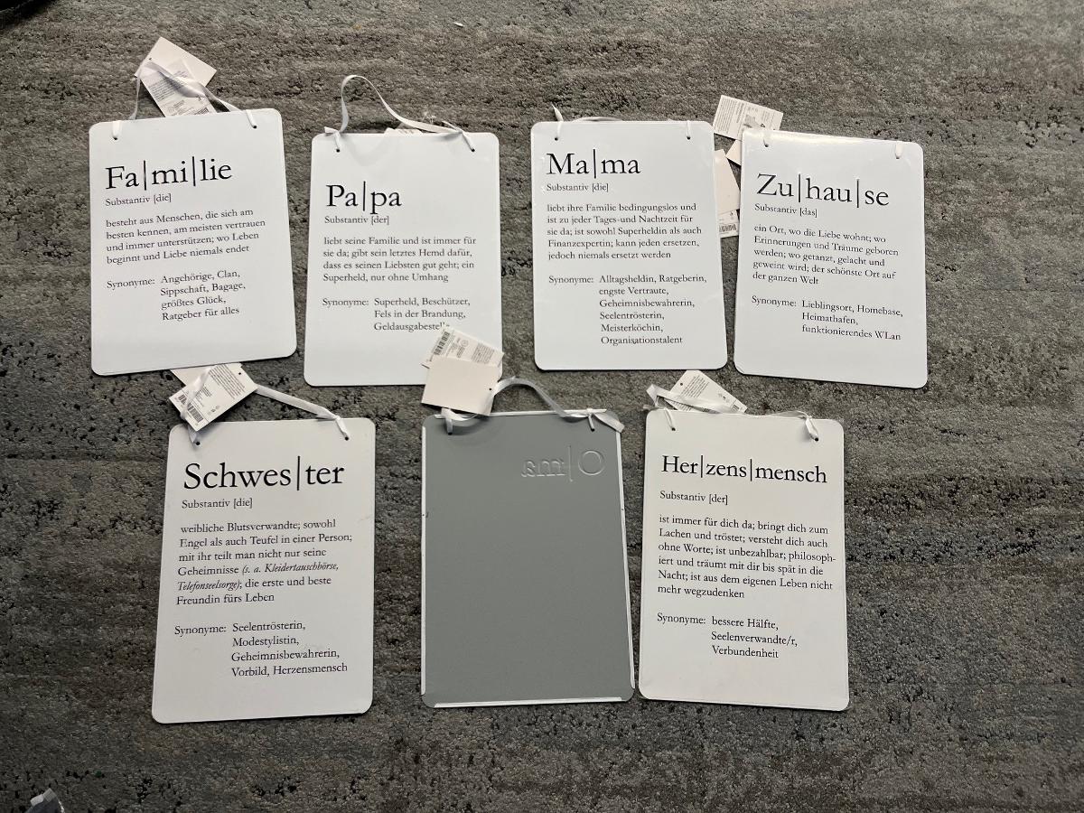 Sogenannte "Blechschilder, mit verschiedenen Texten bedruckt, zum Aufhängen bestimmt":

Es handelt sich um Schilder aus unedlen Metallen, die mit verschiedenartigen Texten bedruckt sind (je nach Variante), am oberen Rand zwei Lochungen aufweisen, durch die ein Aufhängeband aus Spinnstoff gezogen ist. Die Erzeugnisse sind zum Ausschmücken von Innenräumen bestimmt, wobei der Schriftzug zum Lesen animieren soll. So werden z. B. bei den Begriffen "Familie, Papa, Mama, Schwester, Oma" etc. der Wortstamm (Substantiv), Einordnung, Synonyme und deren Bedeutung erläutert.  
- Antragstellerangaben -

Abbildung siehe Anlage.

Kein Schild aus unedlem Metall im Sinne der Position 8310.
Derartige Waren gehören als "andere als in den vorgenannten Unterpositionen KN angeführte Drucke" in die Unterposition 4911 99 00 der Kombinierten Nomenklatur und sodann zum TARIC-Code 4911 9900 00.
