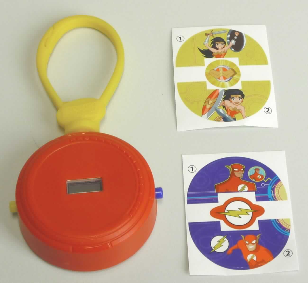 Bei dem Erzeugnis "Stop Watch Clip" aus der Serie "Mc Donals - Justice League 2018" handelt es sich um eine Warenzusammenstellung in Aufmachung für den Einzelverkauf, bestehend aus einer runden, elektrisch (mit Batterie) betriebenen Uhr, in einem Kunststoffgehäuse (Durchmesser: ca. 6 cm, Höhe: ca. 2 cm) mit zwei Drucktasten an den Seiten zum Einstellen der digital angezeigten Uhrzeit und einem Ein-/Auschalter auf der Rückseite sowie einem ca. 7 cm großen Klipp aus Kunststoff auf der Oberseite als Befestigungsmöglichkeit, und zwei verschiedenen, passgenauen Aufklebern zur dekorativen Ausgestaltung der Uhr.

Die Taschenuhr ähnliche Uhr ist aufgrund Umfang und Verwendungszweck charakterbestimmend gegenüber den beiden Aufklebern. 
 
Die in einer durchsichtigen Kunststofftüte verpackte Ware ist als "andere als in der Position 9101 erfasste, den Taschenuhren ähnliche Uhr, elektrisch betrieben" einzureihen.