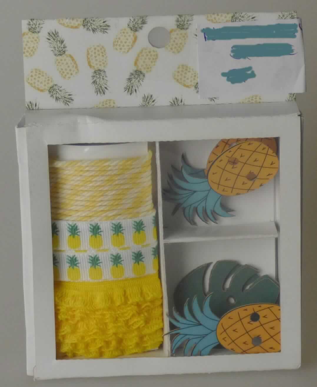 Geschenkverpackung, sog. Geschenkdekoset Ananas, Foto siehe Anlage,
- Warenzusammenstellung, bestehend aus zwei "Geschenkbändern" (einem Band und einem Geflecht), einer 
  "Kordel" sowie vier "Geschenkanhängern",
- zur Befriedigung eines speziellen Bedarfs zusammengestellt und gemeinsam in einer Pappschachtel mit 
  Kunststoffdeckel für den Einzelverkauf aufgemacht,
- "Geschenkbänder":
-- Band:
--- als Meterware, mit einer Breite von ca. 1 cm, 
--- aus bedruckten Geweben aus synthetischen Chemiefasern (laut Antrag Polyester),
--- mit echten Webkanten an beiden Längsseiten,
--- kein Samt, Plüsch, Chenille- oder Schlingengewebe,
--- keine Elastomergarne oder Kautschukfäden enthaltend,
-- Geflecht:
--- wellenförmig, mit einer Breite von ca. 1 cm,
--- aus einem Flachgeflecht aus synthetischen Chemiefasern (laut Antrag Polyester),
- "Kordel":
-- mit einer Länge von ca. 1 m und mit einer Breite von ca. 0,2 mm,
-- aus synthetischen Chemiefasern (laut Antrag Polyester),
-- gezwirnt, mit einer S-Drehung als letzter Drehung, 
-- an beiden Enden mit einer Hülse aus Kunststoff eingefasst (konfektioniert),
- "Geschenkanhänger":
-- in Form eines Blattes und einer Ananas, in den Abmessungen von ca. 2,7 cm bzw. 3 cm x 3,8 cm bzw. 4,7 cm,
-- aus Papier,
-- in der Mitte mit einer Aufhängevorrichtung,
- im Hinblick auf die Bedeutung in Bezug auf die Verwendung sind alle Bestandteile als gleich zu betrachten, im
  Hinblick auf den Wert jedoch verleiht das Band der Warenzusammenstellung den wesentlichen Charakter.

"Band, keine Ware der Position 5807, kein Samt, Plüsch, Chenille- oder Schlingengewebe, keine Elastomergarne 
 oder Kautschukfäden enthaltend, aus Chemiefasern, mit echten Webkanten"