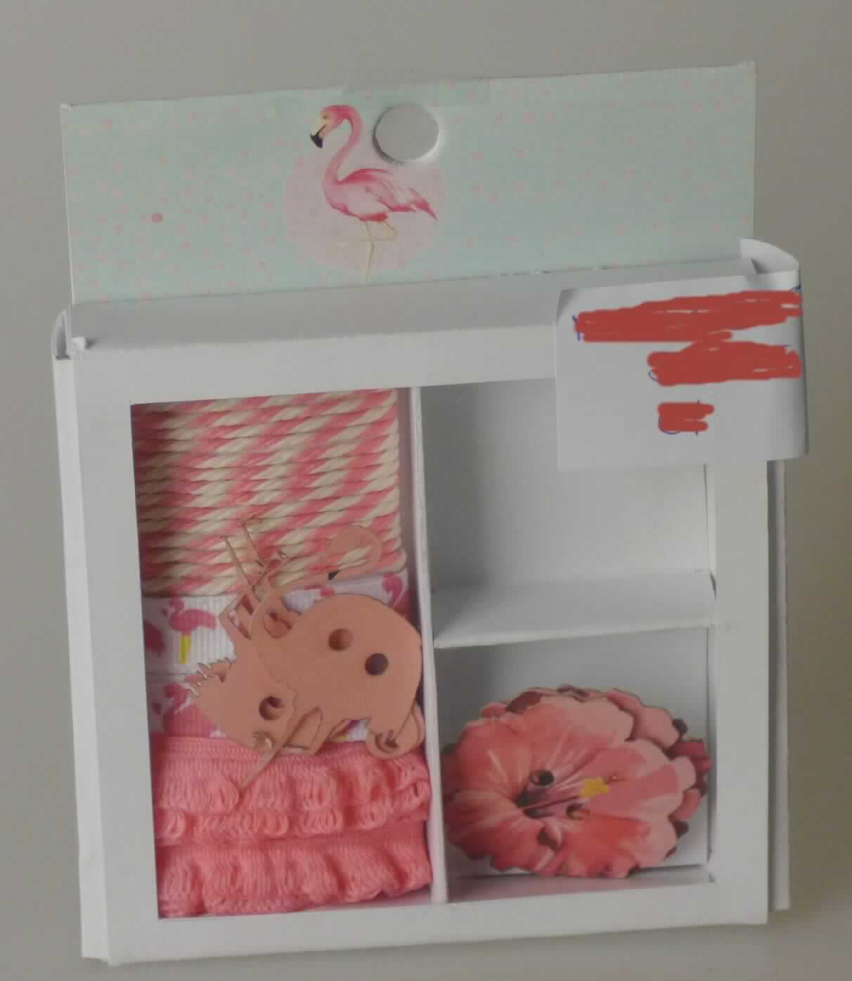 Geschenkverpackung, sog. Geschenkdekoset Flamingo, Foto siehe Anlage,
- Warenzusammenstellung, bestehend aus zwei "Geschenkbändern" (einem Band und einem Geflecht), einer 
  "Kordel" sowie vier "Geschenkanhängern",
- zur Befriedigung eines speziellen Bedarfs zusammengestellt und gemeinsam in einer Pappschachtel mit 
  Kunststoffdeckel für den Einzelverkauf aufgemacht,
- "Geschenkbänder":
-- Band:
--- als Meterware, mit einer Breite von ca. 1 cm, 
--- aus bedruckten Geweben aus synthetischen Chemiefasern (laut Antrag Polyester),
--- mit echten Webkanten an beiden Längsseiten,
--- kein Samt, Plüsch, Chenille- oder Schlingengewebe,
--- keine Elastomergarne oder Kautschukfäden enthaltend,
-- Geflecht:
--- wellenförmig, mit einer Breite von ca. 1 cm,
--- aus einem Flachgeflecht aus synthetischen Chemiefasern (laut Antrag Polyester),
- "Kordel":
-- mit einer Länge von ca. 1 m und mit einer Breite von ca. 0,2 mm,
-- aus synthetischen Chemiefasern (laut Antrag Polyester),
-- gezwirnt, mit einer S-Drehung als letzter Drehung, 
-- an beiden Enden mit einer Hülse aus Kunststoff eingefasst (konfektioniert),
- "Geschenkanhänger":
-- in Form einer Blüte und eines Flamingos, in den Abmessungen von ca. 2,9 cm bzw. 3,5 cm x 3,5 cm bzw. 4 cm,
-- aus Papier,
-- in der Mitte mit einer Aufhängevorrichtung,
- im Hinblick auf die Bedeutung in Bezug auf die Verwendung sind alle Bestandteile als gleich zu betrachten, im
  Hinblick auf den Wert jedoch verleiht das Band der Warenzusammenstellung den wesentlichen Charakter.

"Band, keine Ware der Position 5807, kein Samt, Plüsch, Chenille- oder Schlingengewebe, keine Elastomergarne 
 oder Kautschukfäden enthaltend, aus Chemiefasern, mit echten Webkanten"