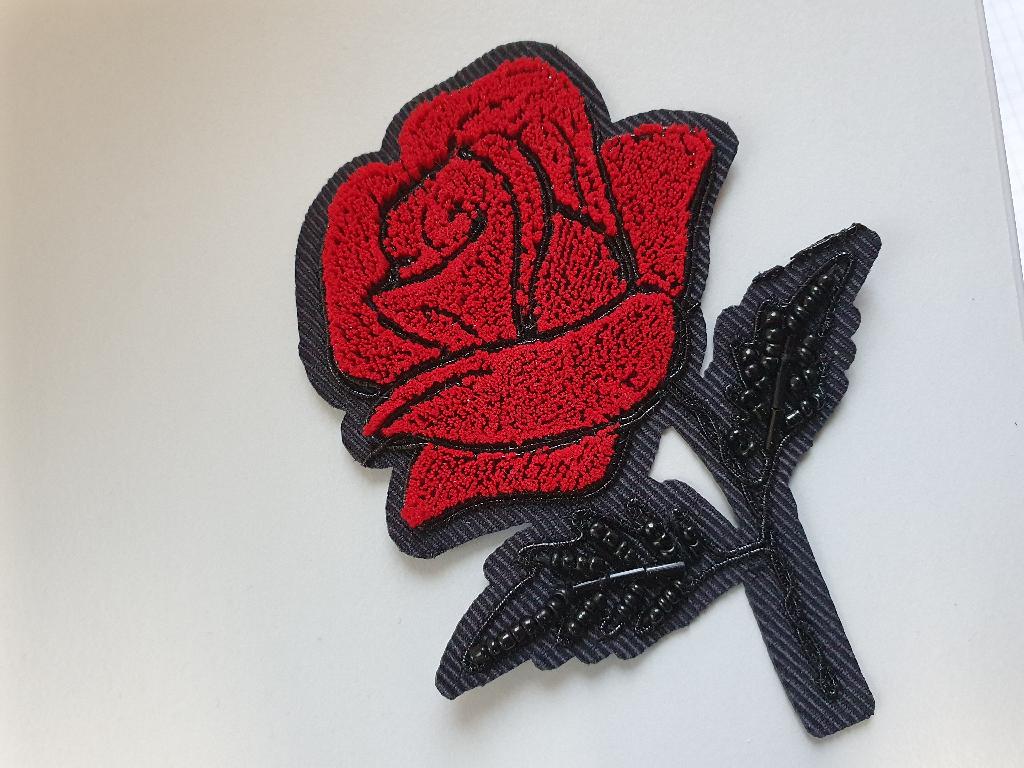 Stickereien als Motiv, Foto siehe Anlage, 
- in den Abmessungen von ca. 8 cm x 10 cm,
- mit einem Stickgrund aus Gewebe aus laut Antrag Chemiefasern, 
- mit Stickgarnen und Perlen aus laut Antrag Kunststoff bestickt, 
- keine Ätzstickerei oder Stickerei mit herausgeschnittenem Grund,
- auf der Rückseite mit einem Kleber aus Kunststoff ausgestattet, 
- laut Antrag mit einem Wert von weniger als 17,50 EUR je kg Eigengewicht, 
- ohne Hinweise auf Handarbeit.

"Stickereien als Motiv, andere als Ätzstickereien und Stickereien mit herausgeschnittenem Grund, aus 
 Chemiefasern, mit einem Wert von weniger als 17,50 EUR je kg Eigengewicht, nicht handgearbeitet"